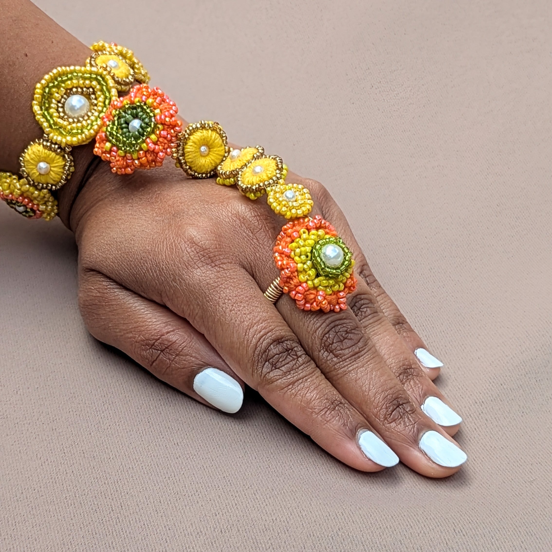 Hand wearing a haldi inspired yellow, orange, green, seed pearl Indian hand bracelet by Mayaani Jewellery UK handcrafted in celebration of heritage, connection and sustainability.