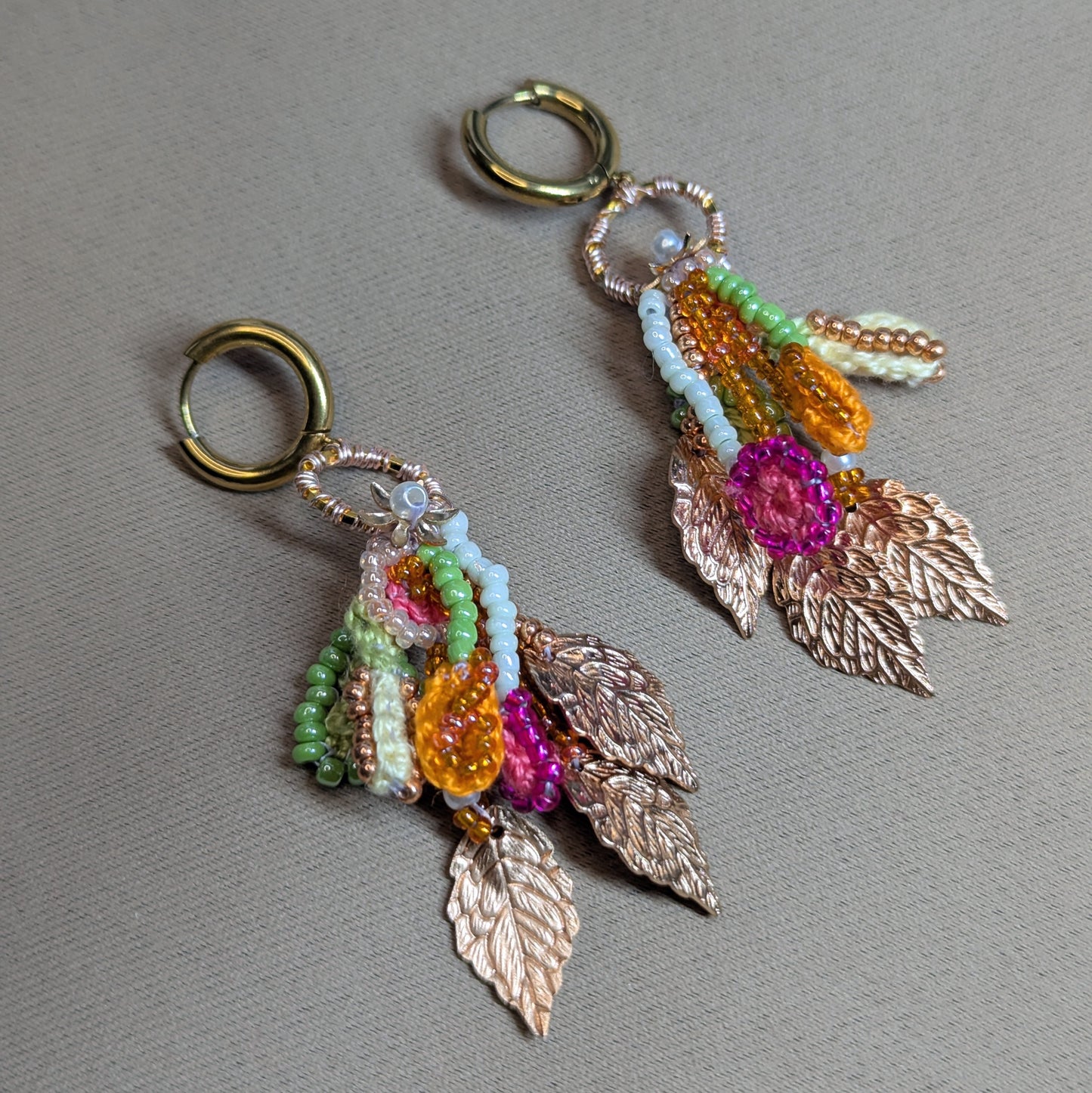 Zariya earrings laid on fabric, showcasing cascading rose gold leaves and colourful bead-and-cotton textures inspired by a spring garden in rainfall.