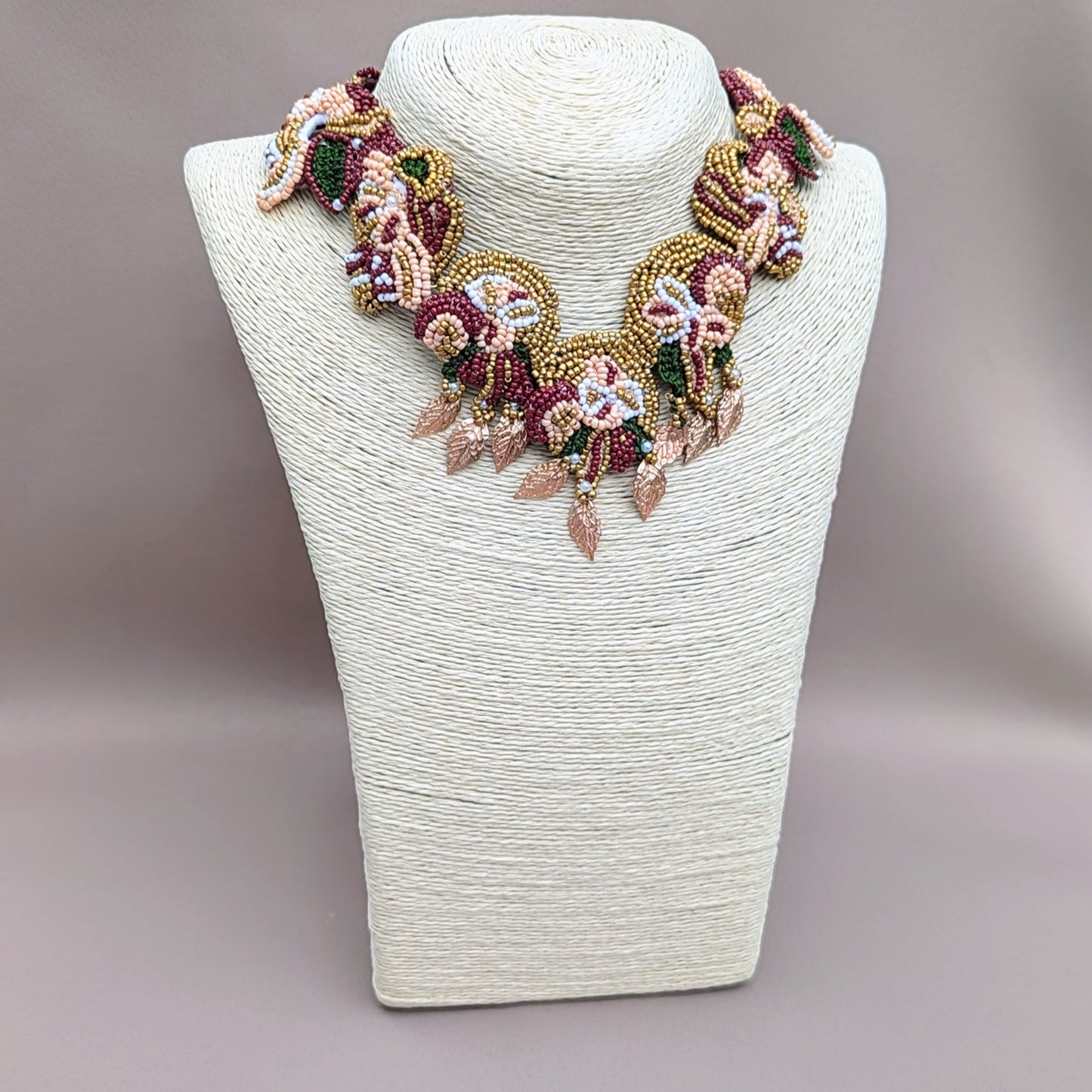 Close-up of Aishwarya necklace showing red, green and gold beadwork with fine silver wire wrapping and gold accents.