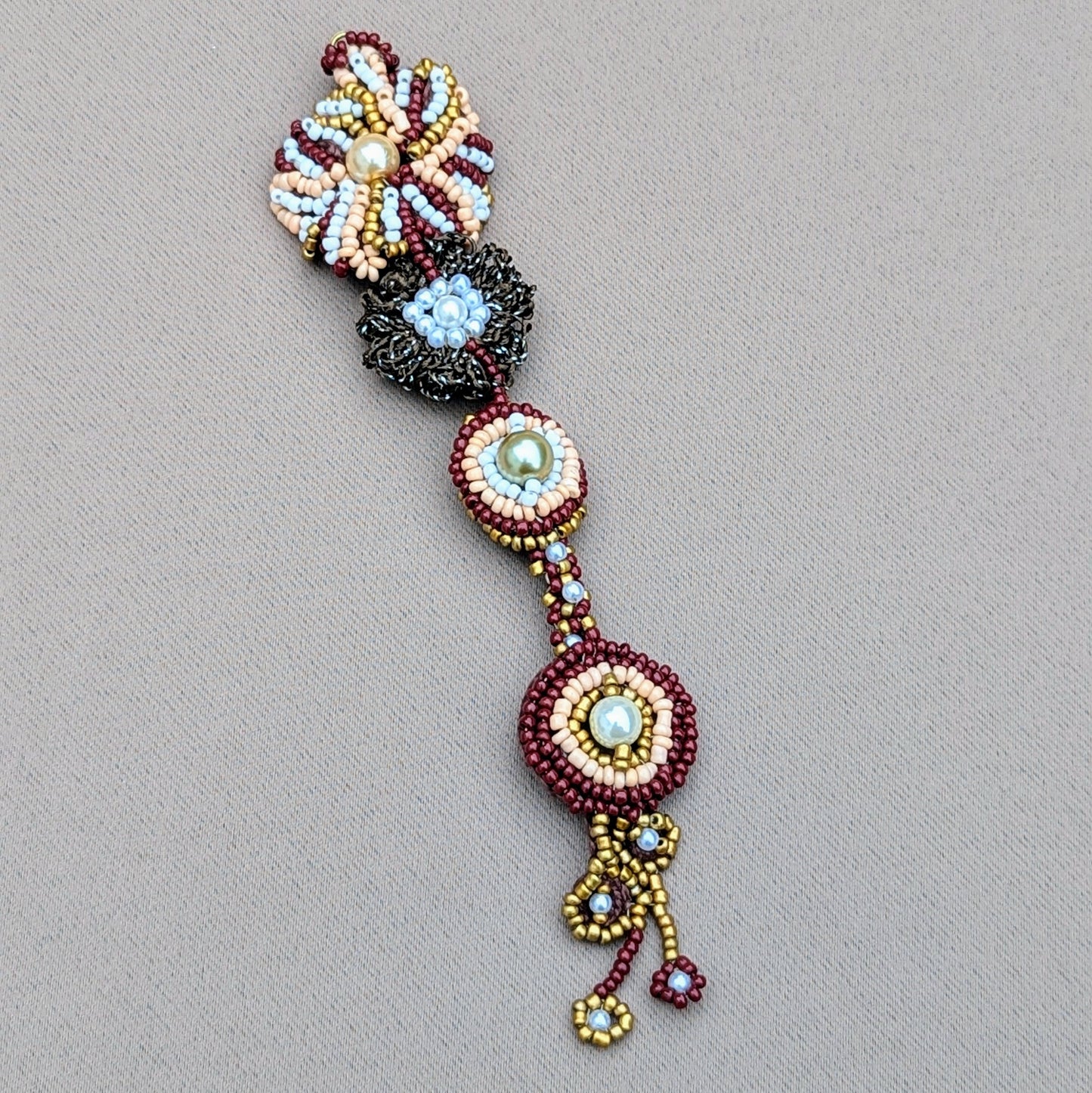 Aishwarya maang tikka exclusive to Mayaani Jewellery UK and hand-crocheted and beaded in rich hues of deep brick red, gold, pearly white, and earthy greens and browns, showcasing exceptional craftsmanship and artistry.