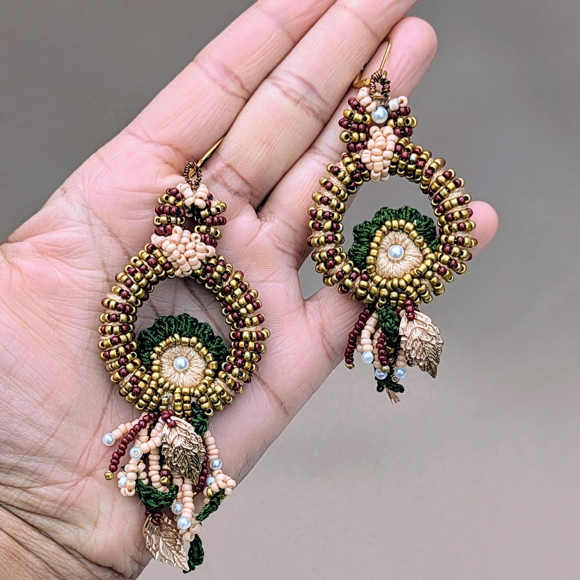 Close-up of Aishwarya bridal earrings showing intricate bead embroidery and traditional Indian colour palette of red, green and gold.