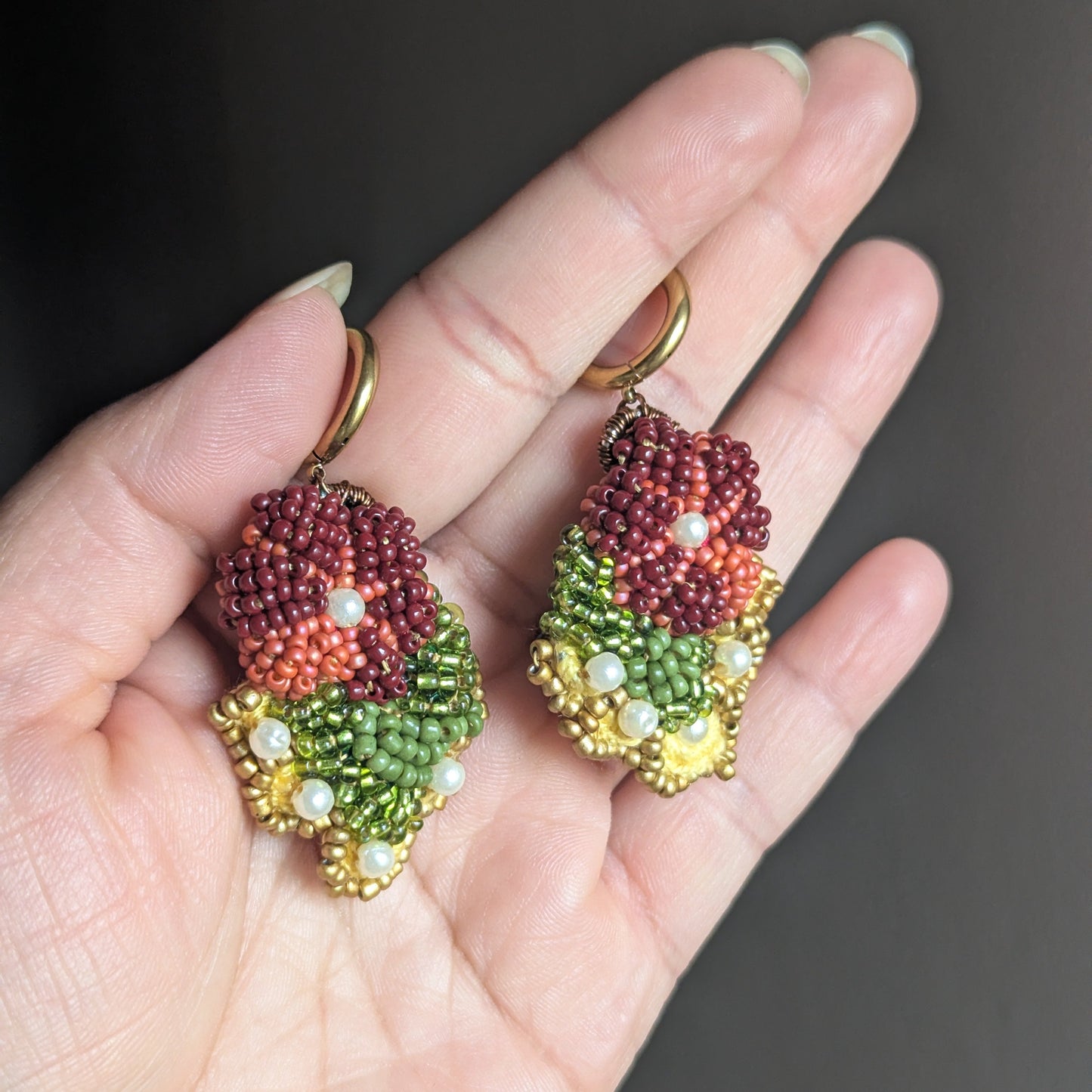 Colourful burgundy, yellow, olive green, pearl and gold statement Indian earrings sustainable handcrafted at Mayaani Jewellery UK - held in hand against neutral grey backdrop.