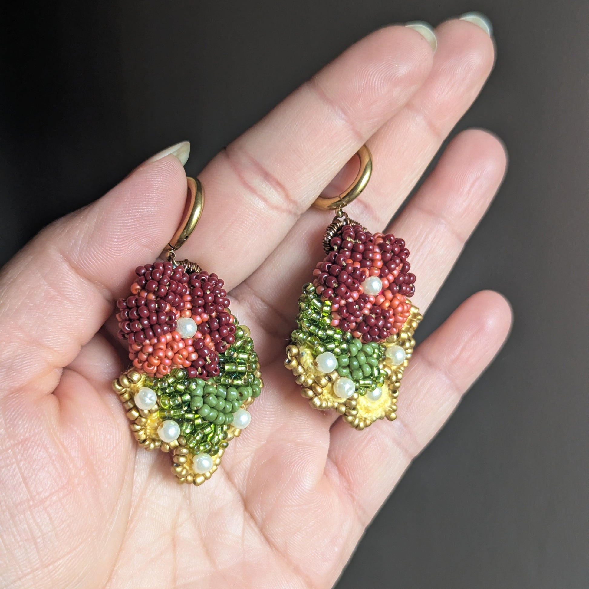 Colourful burgundy, yellow, olive green, pearl and gold statement Indian earrings sustainable handcrafted at Mayaani Jewellery UK - held in hand against neutral grey backdrop.