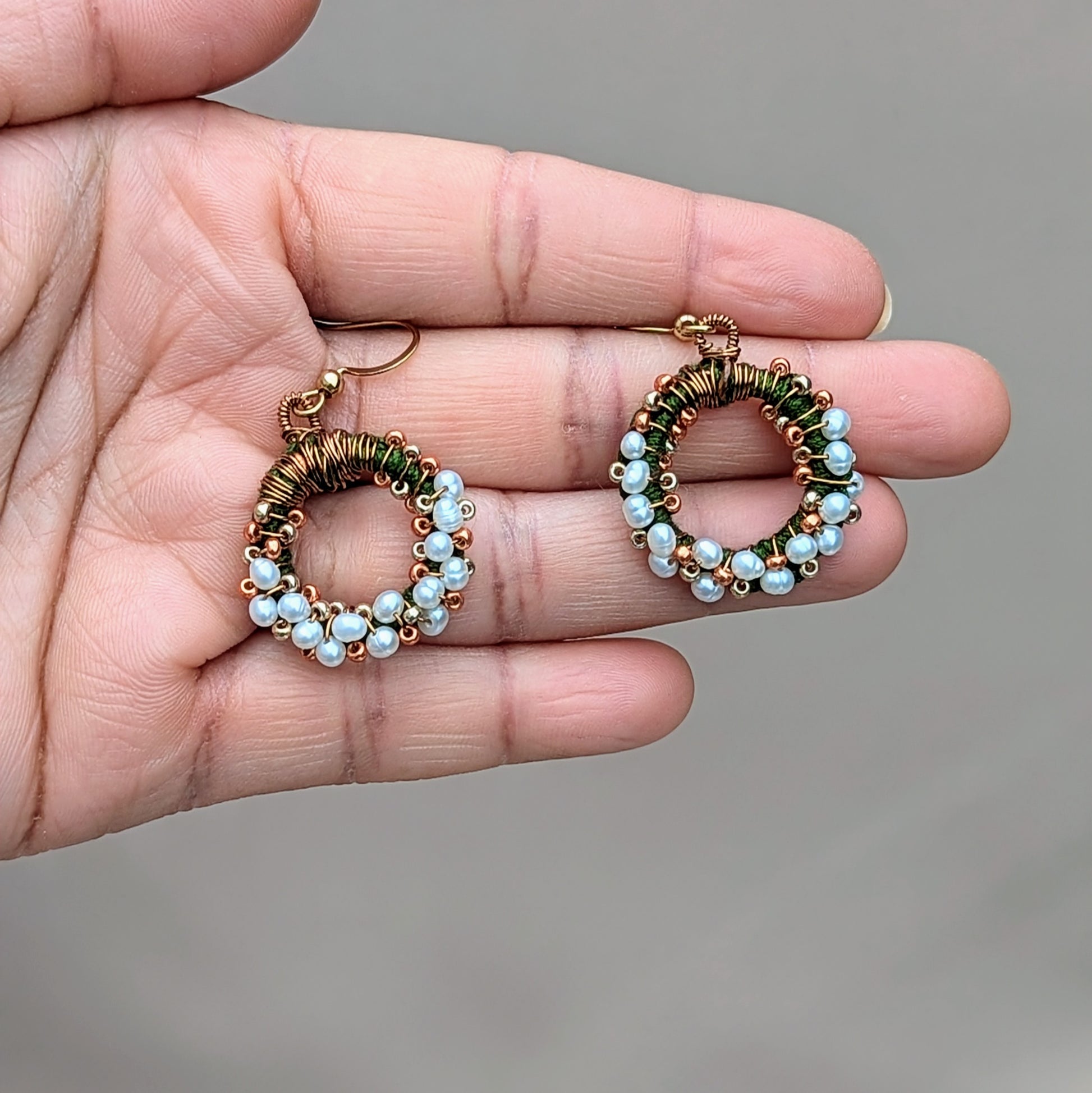 A limited edition design exclusive to Mayaani Jewellery UK, these handcrafted freshwater pearl earrings feature green crochet, antique bronze wire wrapping, and gold beadwork in a circular motif. Gold-plated stainless steel hooks complete the look, offering an Indian-inspired twist on timeless pearls, ideal for special occasions through to everyday.