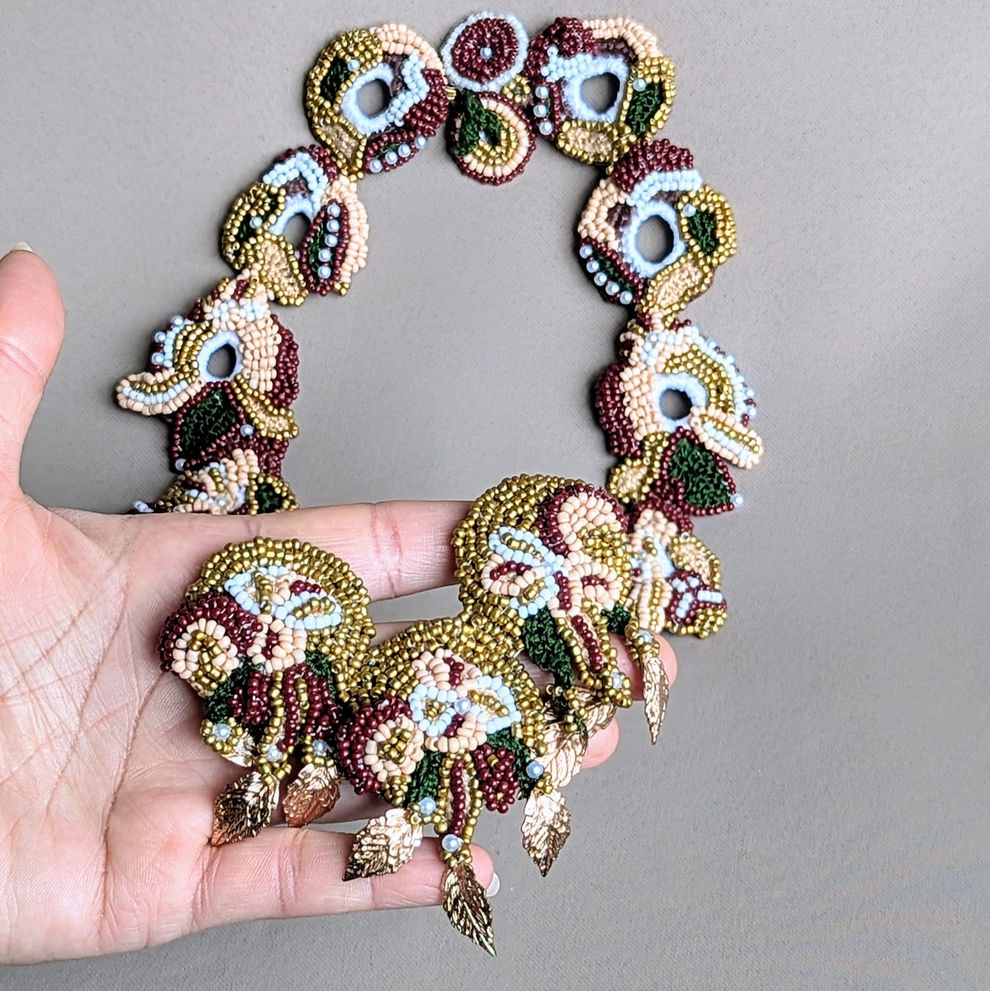 Hand holding Aishwarya necklace displaying detachable centrepiece and complementary green crochet chain.