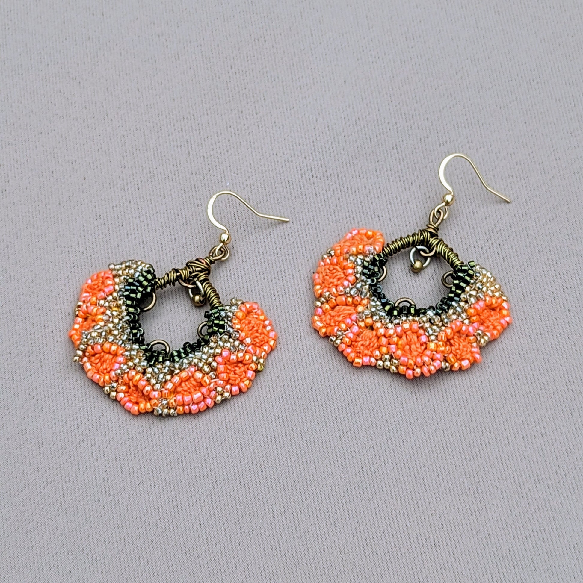 Discover a vibrant pair of Indian earrings in bold orange, green, and gold, exclusively from the sustainable UK brand Mayaani Jewellery. These earrings feature a lovely brass bead that hangs elegantly from hand-wrapped bronze copper wire, creating joyful movement within the floral fan-like design. Ideal for special occasions or everyday wear, they add a touch of joy to any outfit.