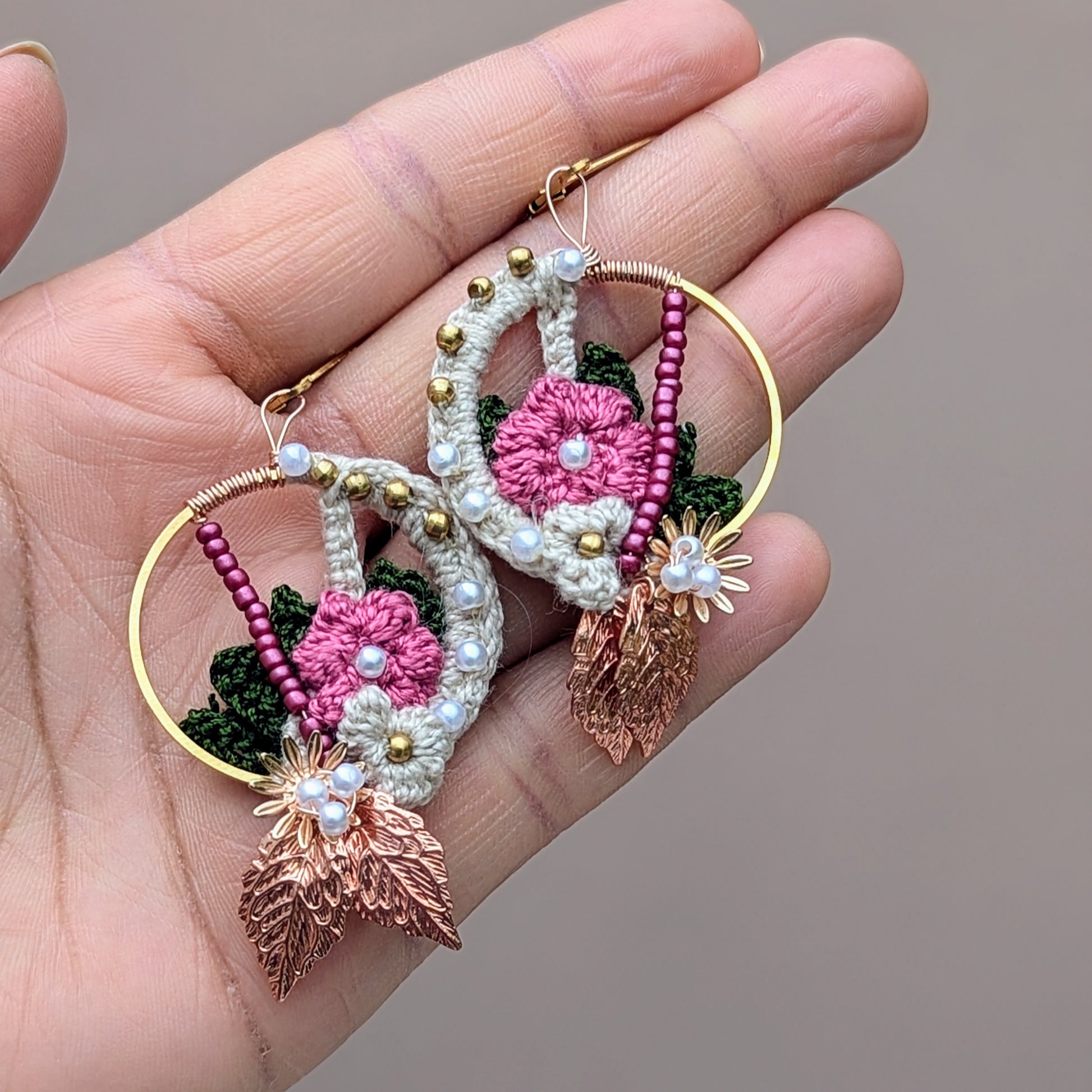 Pictured in the palm of a hand, discover handcrafted Indian-inspired earrings from Mayaani Jewellery, a sustainable UK brand. These exclusive pieces feature a lovely blend of cream, pink, and dark green floral and leaf elements, adorned with solid brass, pink, and seed pearl beads. Finished with rose gold leaves and gold-plated stainless steel clasps, they offer a lightweight, eye-catching design perfect for weddings, special occasions, or daily wear.