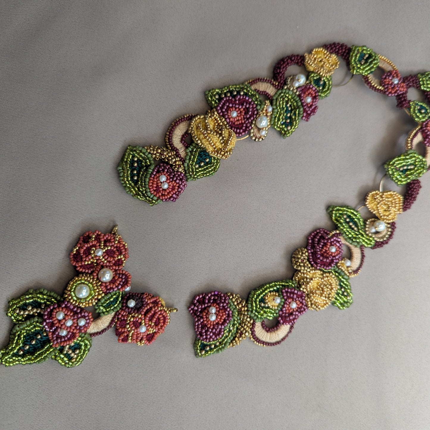 Flat lay view of the Rukmini 2-in-1 couture bridal, wedding necklace hand woven for Mayaani Jewellery UK. Pictured to showcase the central detachable front-facing clasp and intricate workmanship in burgundy, gold, yellow, emerald and olive green.