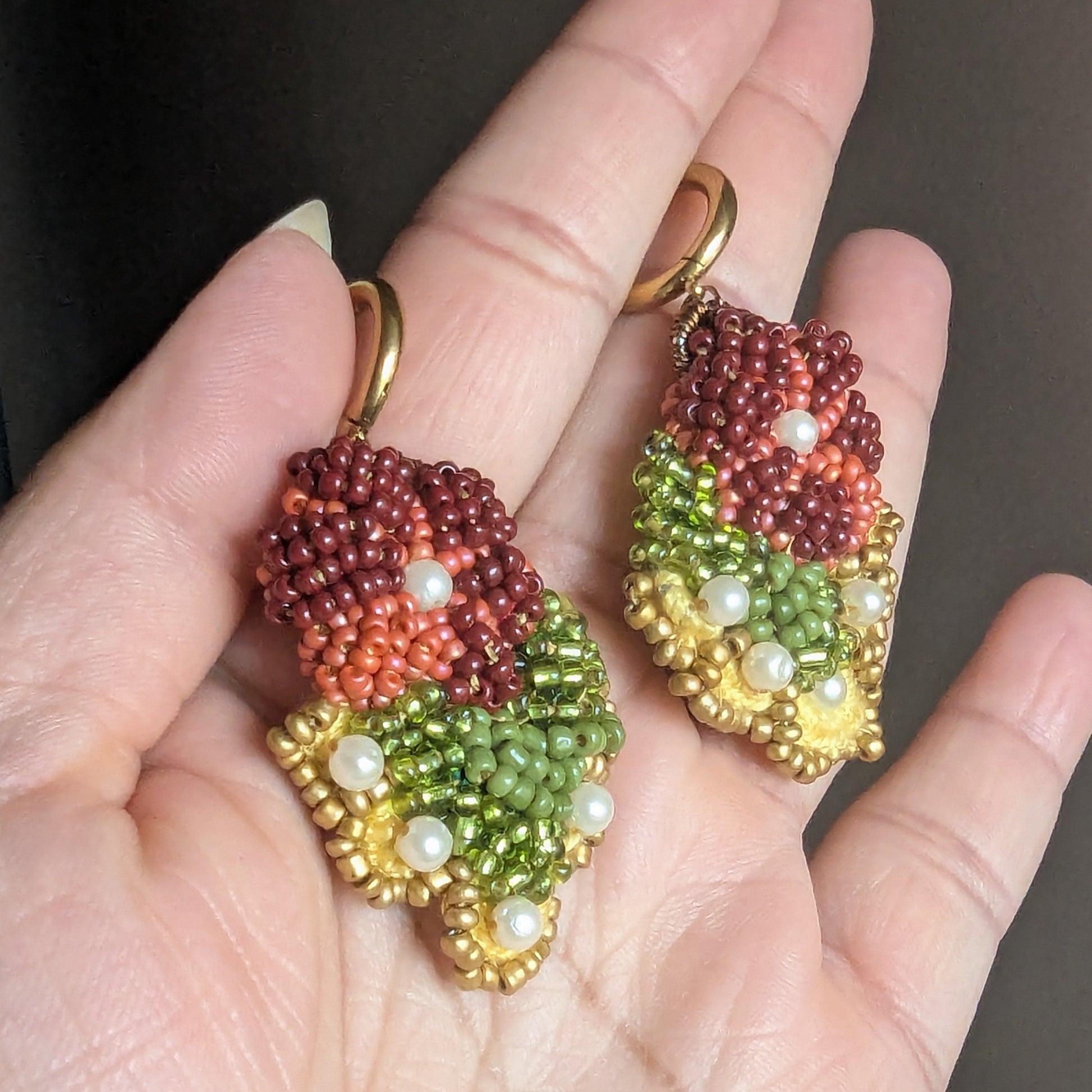 Rukmini handmade beaded drop burgundy, olive green and gold Indian earrings displayed on open palm and exclusive to luxury UK jewellery brand Mayaani Jewellery.