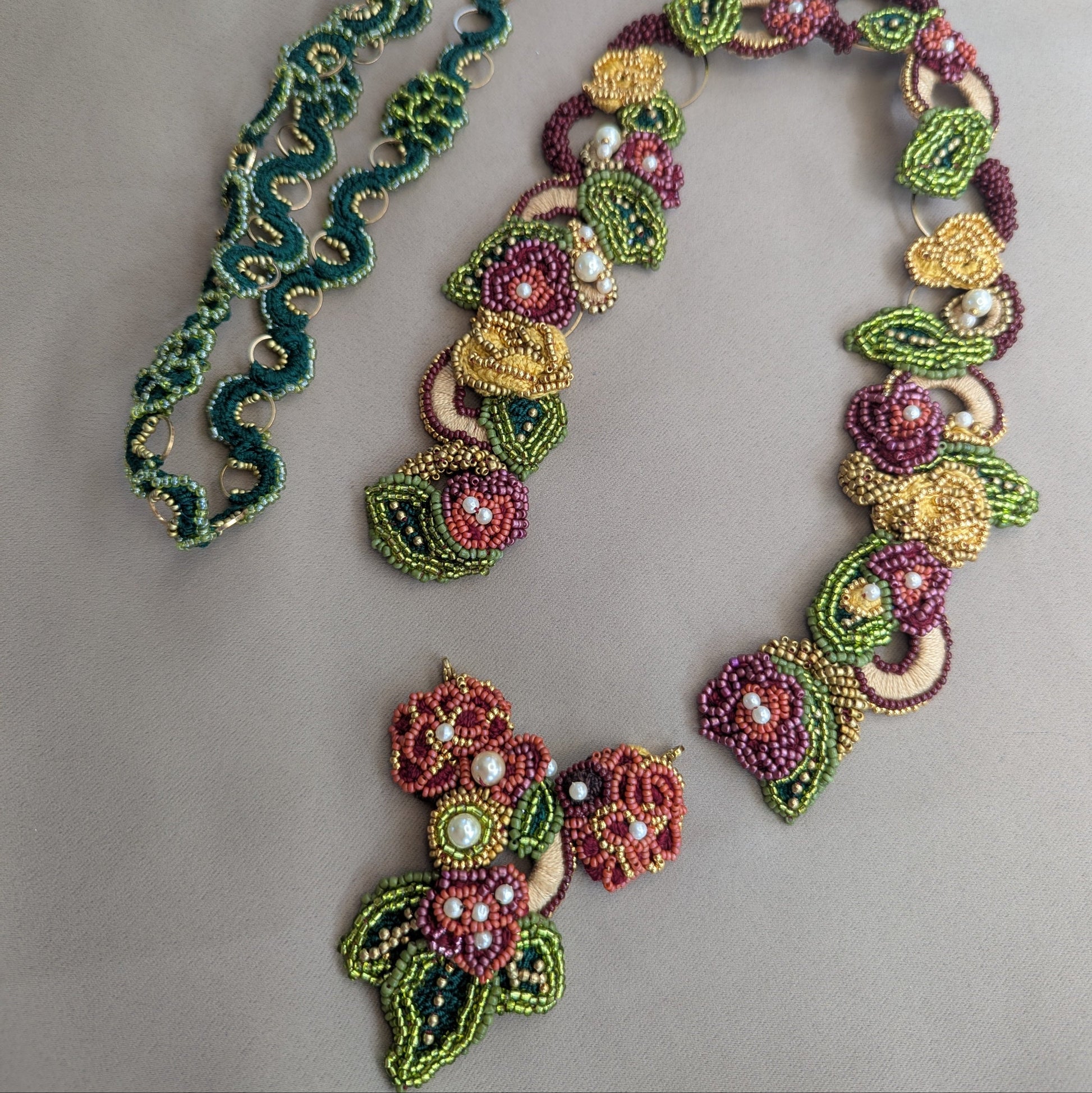  Flat lay of the Rukmini 2-in-1 couture Indian artisan handcrafted emerald green, olive green, gold, yellow and red beaded necklace featuring detachable front facing pendant clasp which can be worn with the Rukmini custom made chain in emerald green and gold pictured folded.