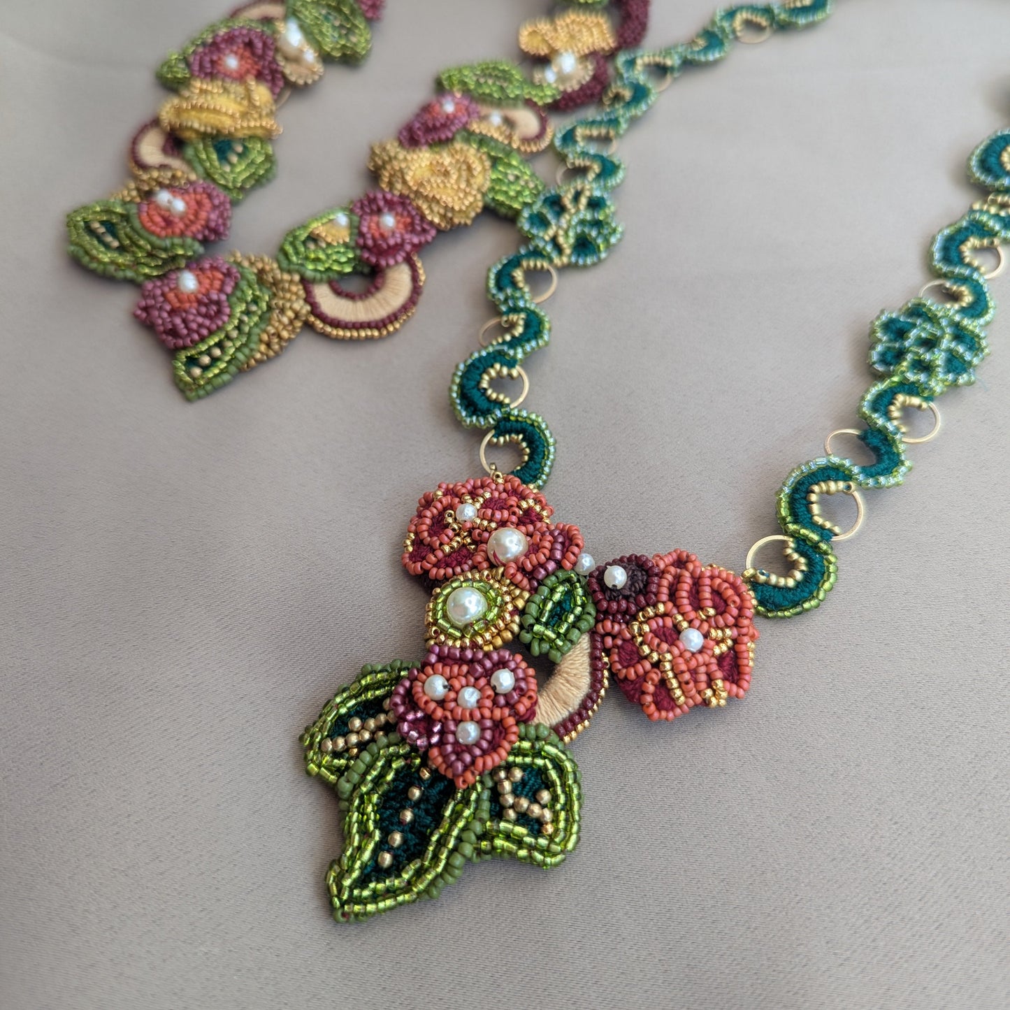 Close up flat lay image of the Mayaani Jewellery Rukmini detachable red, green and gold couture pendant featuring hand bead embroidery, hand crochet and upcycled pearl detailing for sustainable luxury inspired by the modern diaspora woman.