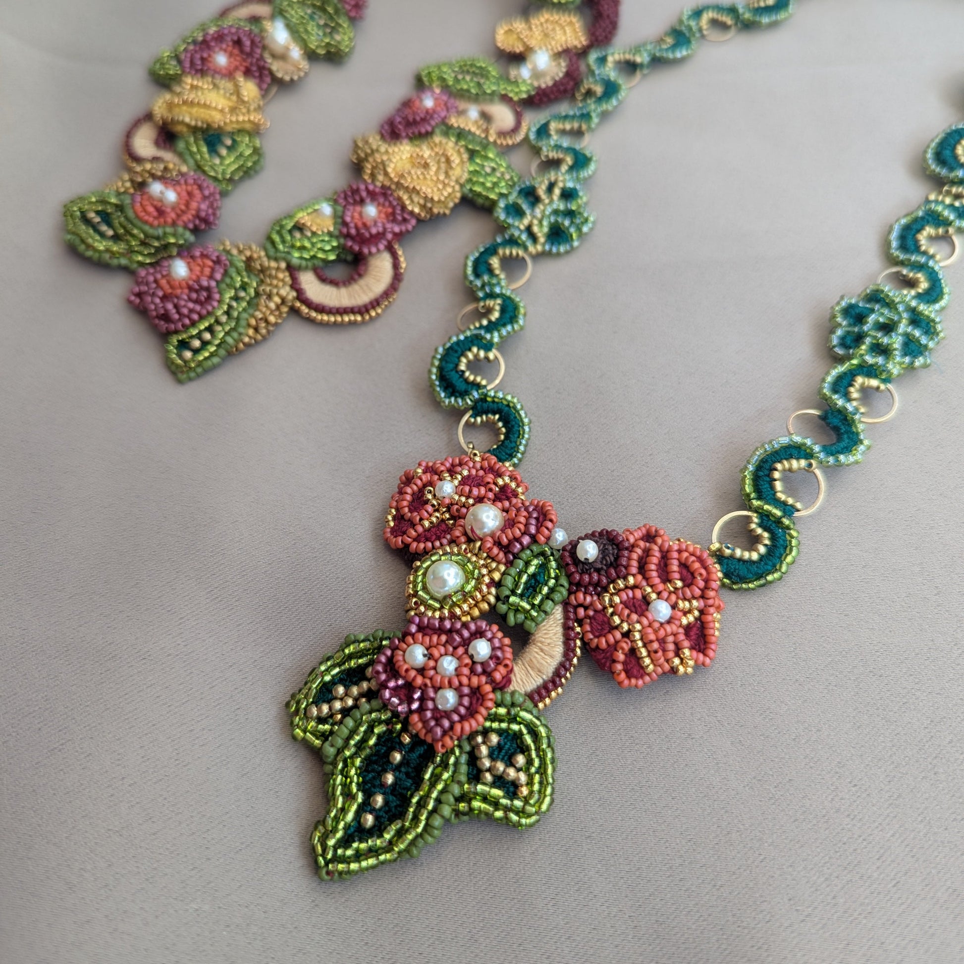 Close up flat lay image of the Mayaani Jewellery Rukmini detachable red, green and gold couture pendant featuring hand bead embroidery, hand crochet and upcycled pearl detailing for sustainable luxury inspired by the modern diaspora woman.