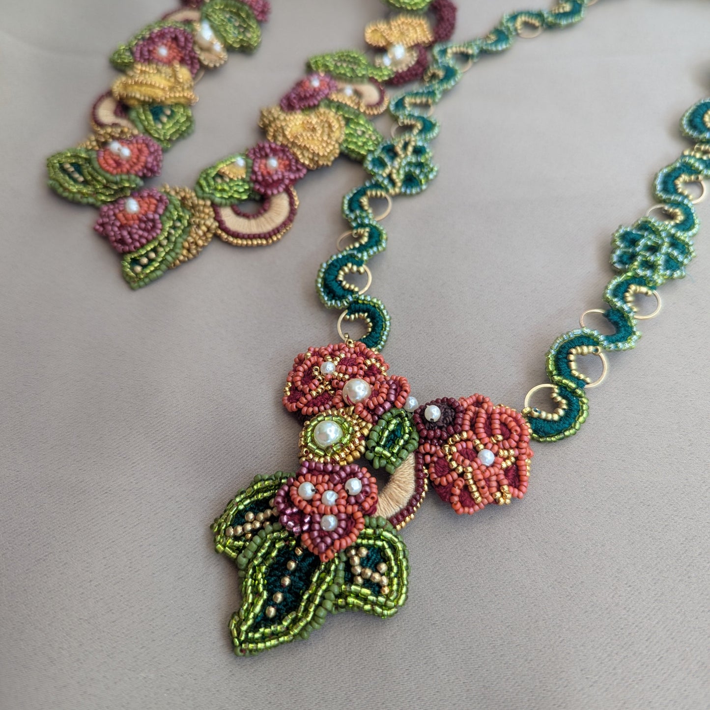 Close up view of the one-of-a-kind Rukmini front facing detachable pendant clasp with the custom made Rukmini emerald green and gold hoop chain on a neutral grey backdrop. The Rukmini statement necklace chain is visible in the top left corner.