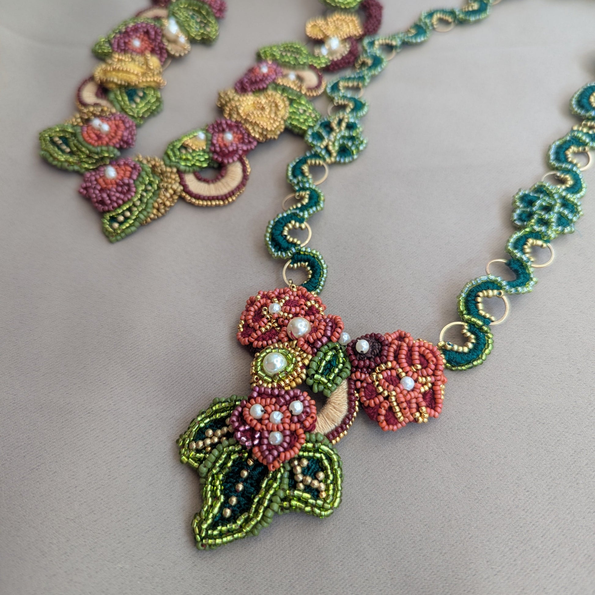 Close up view of the one-of-a-kind Rukmini front facing detachable pendant clasp with the custom made Rukmini emerald green and gold hoop chain on a neutral grey backdrop. The Rukmini statement necklace chain is visible in the top left corner.