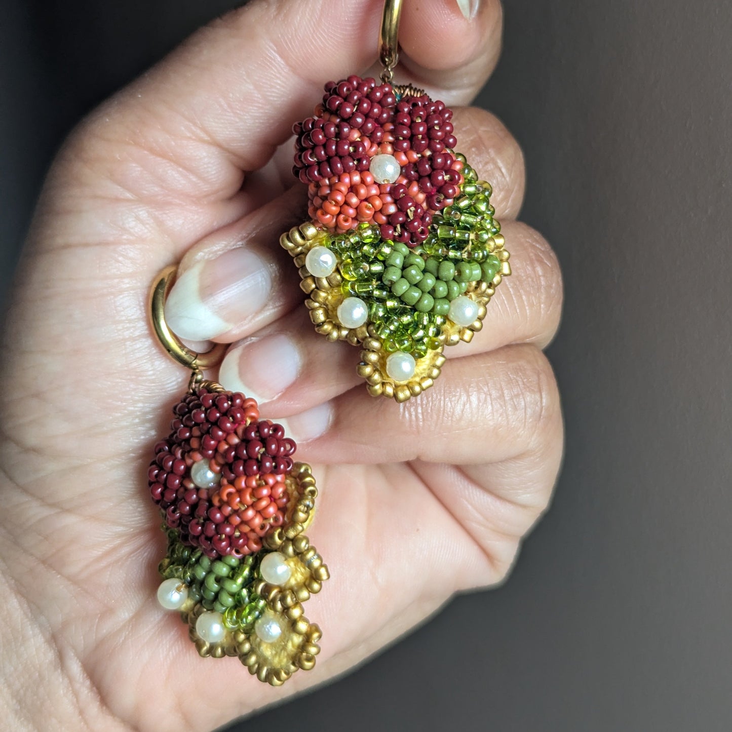 Rukmini handmade beaded drop earrings held in hand - burgundy, olive green and gold Czech glass seed beads with upcycled pearl detail by Mayaani Jewellery UK.