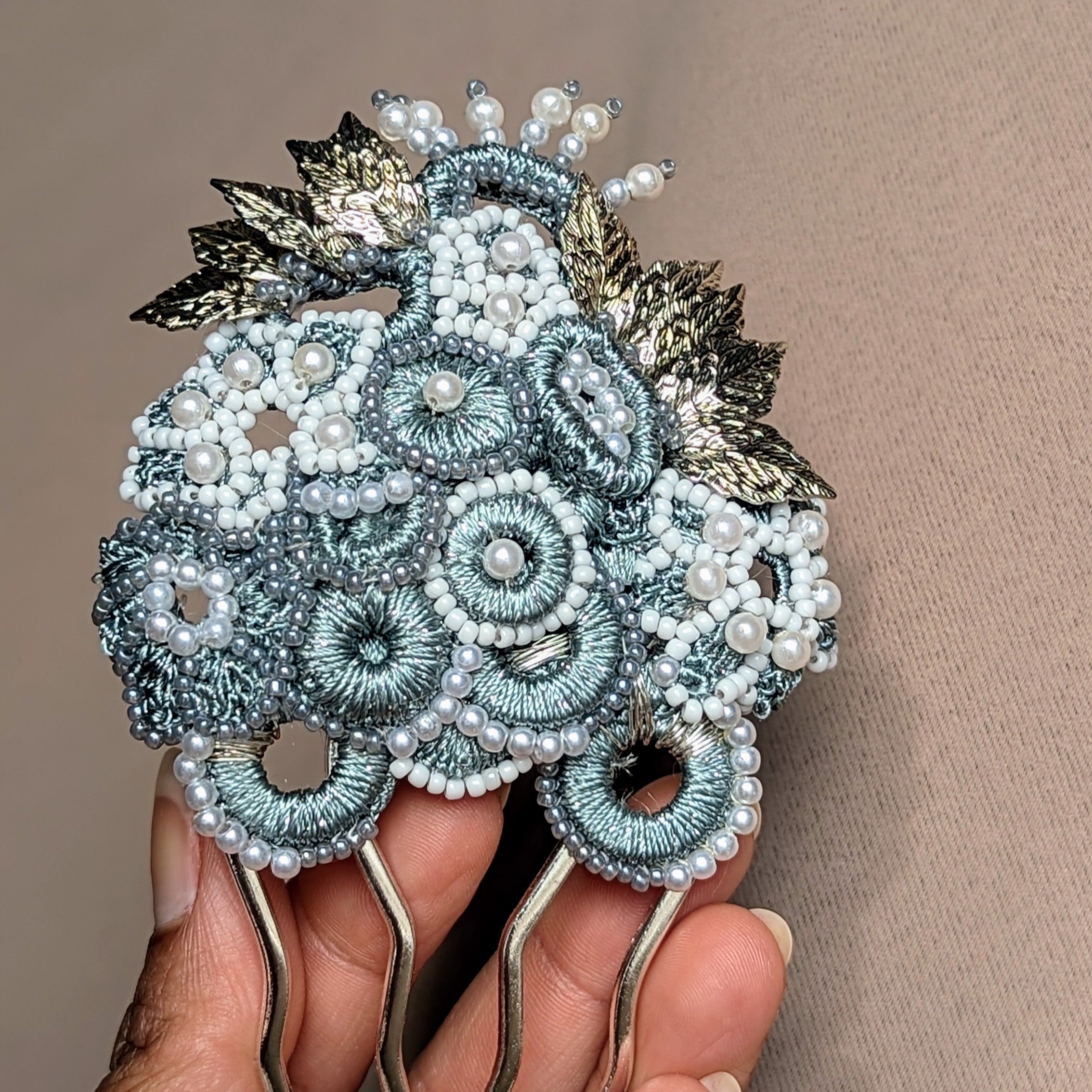 A one of a kind artisan handcrafted Indian inspired bridal hair pin by sustainable UK brand Mayaani Jewellery. Featuring overlapping grey circular and floral motif crochet elements with hand beaded white and ivory seed pearl accents topped with detailed silver plated leaves for a vintage inspired hair accessory reminiscent of ancient royals.