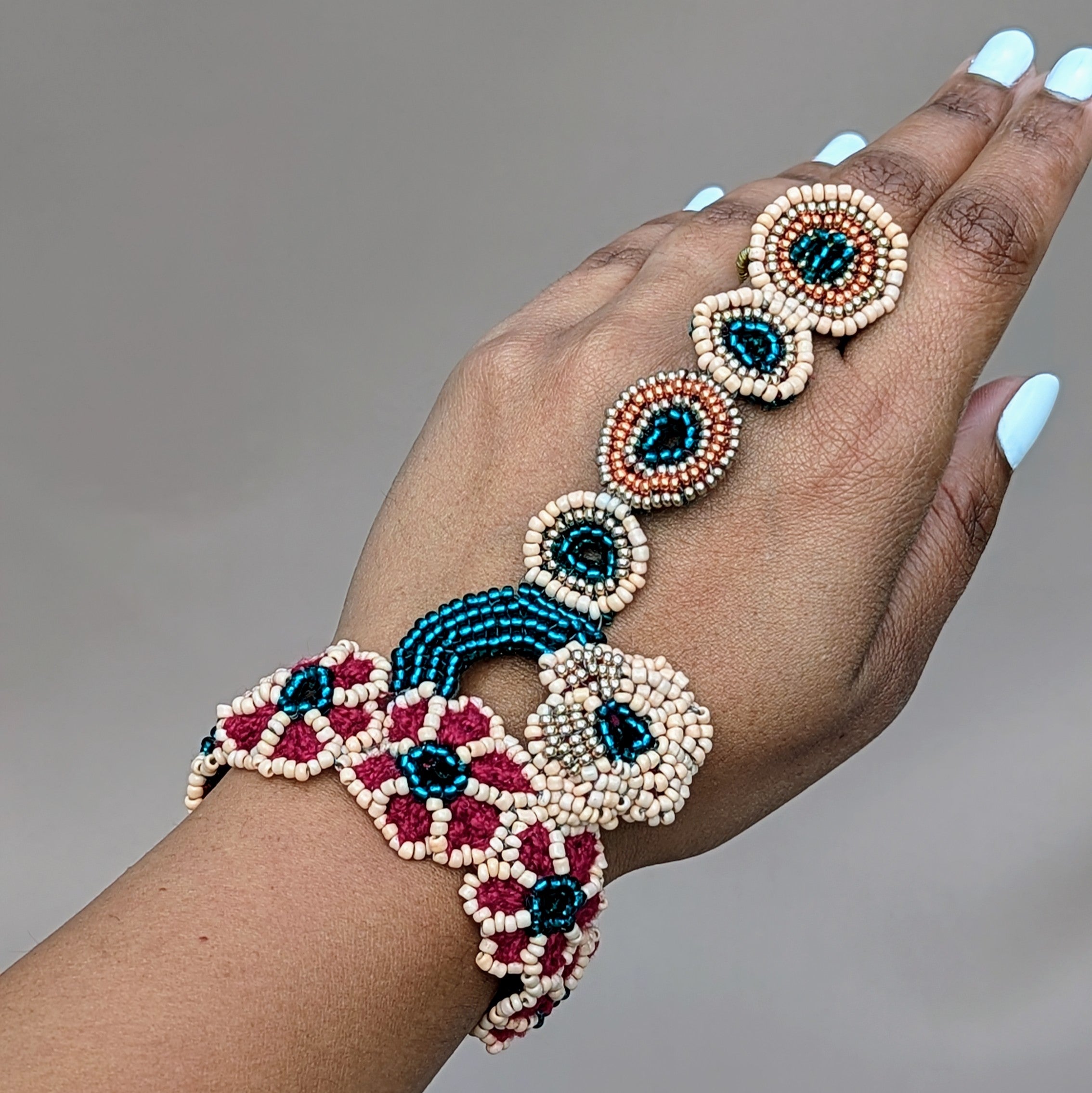Hand modelling a red, emerald green, peach and gold Indian hand bracelet exclusive to sustainable UK brand Mayaani Jewellery for wedding and occasion jewellery perfect for the modern woman who values her culture, embraces style and makes sustainable lifestyle choices.
