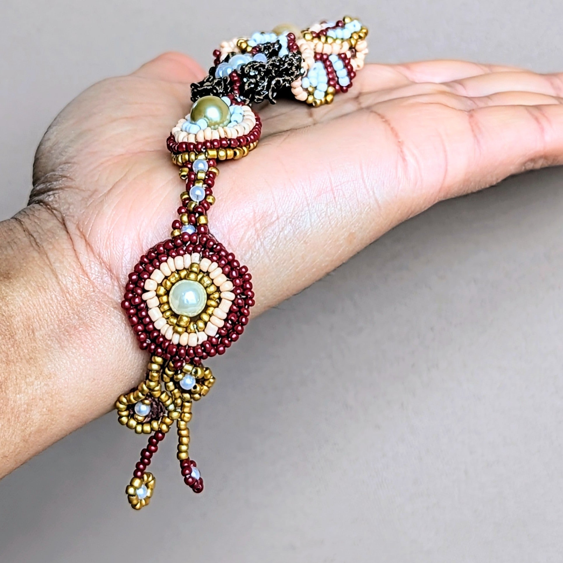 Close-up of an artisan handcrafted Indian bridal tikka from Mayaani Jewellery featuring hand bead embroidery, hand crochet and wire wrapping artistry in rich modern shades of red, green and gold for a sophisticated twist on traditional Indian bridal colours. Ethically handcrafted in the UK for the modern South Asian bride.