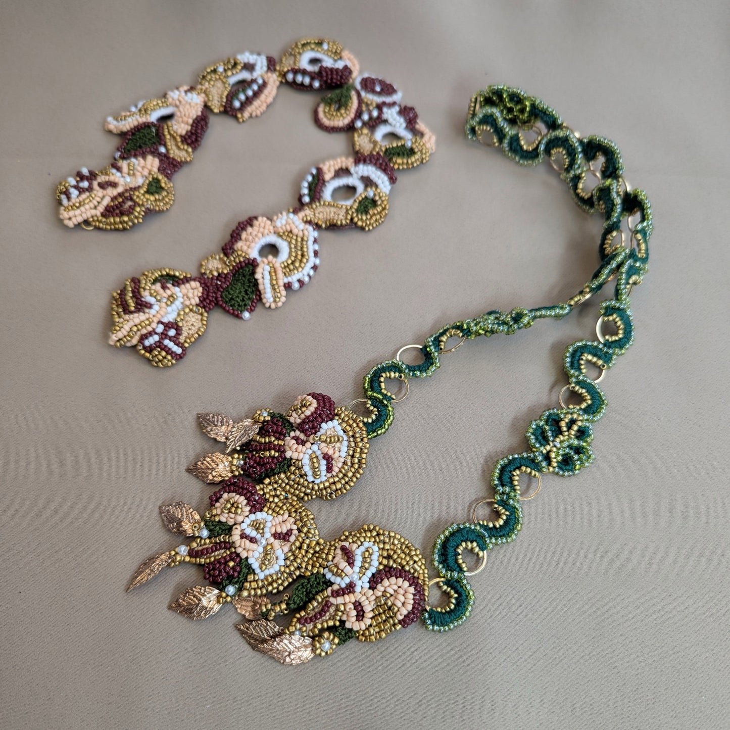 Flat lay view of the detachable statement Aishwarya couture pendant, the Rukmini emerald green and gold custom order chain and the Aishwarya statement bridal neck chain on a neutral grey backdrop.
