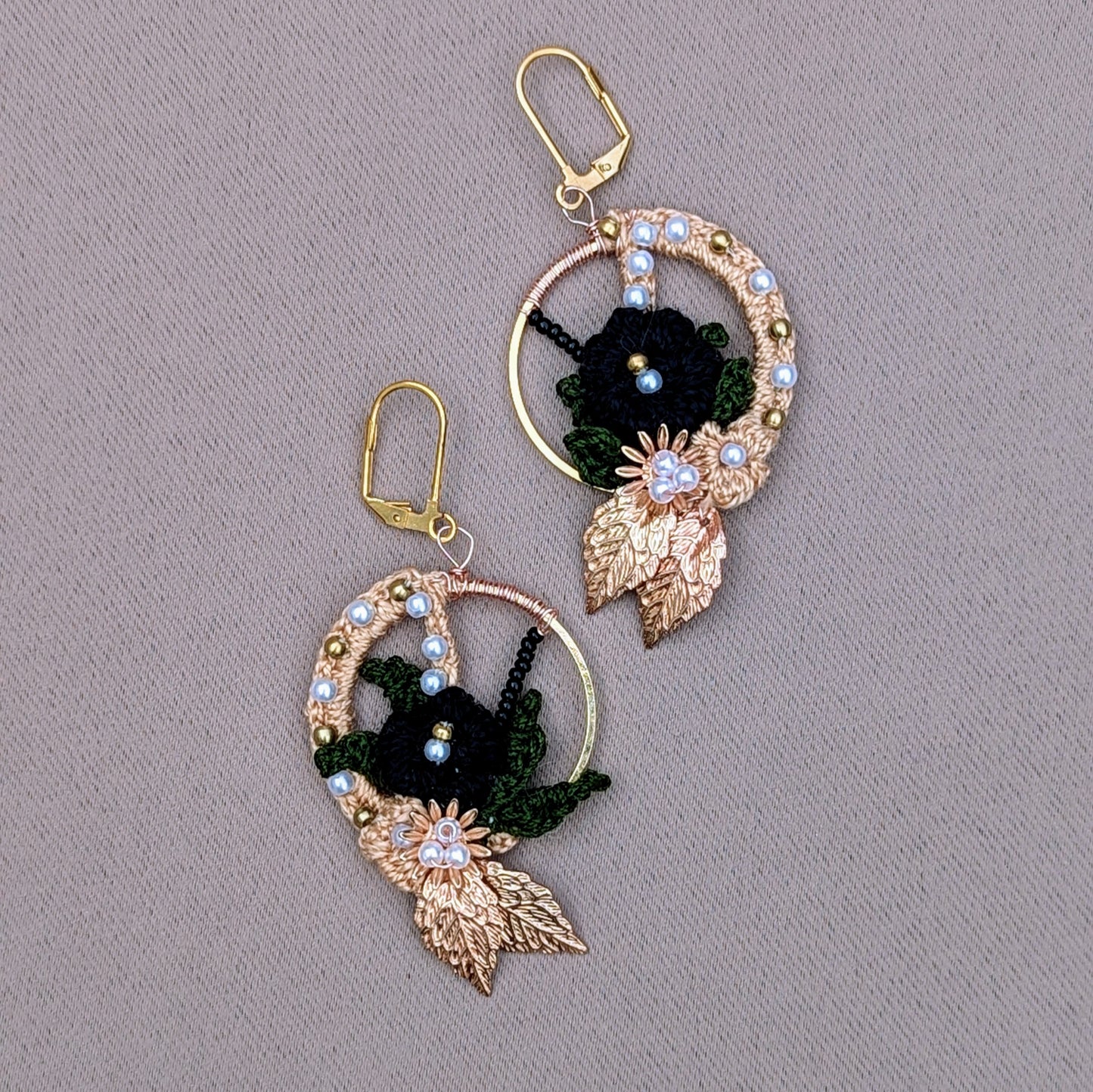 One-of-a-kind Aloki black and gold hoop earrings with floral motif, handcrafted in crochet using black and olive green threads, accented with gold-plated leaves, solid brass beads, and seed pearls, designed by Mayaani Jewellery UK.