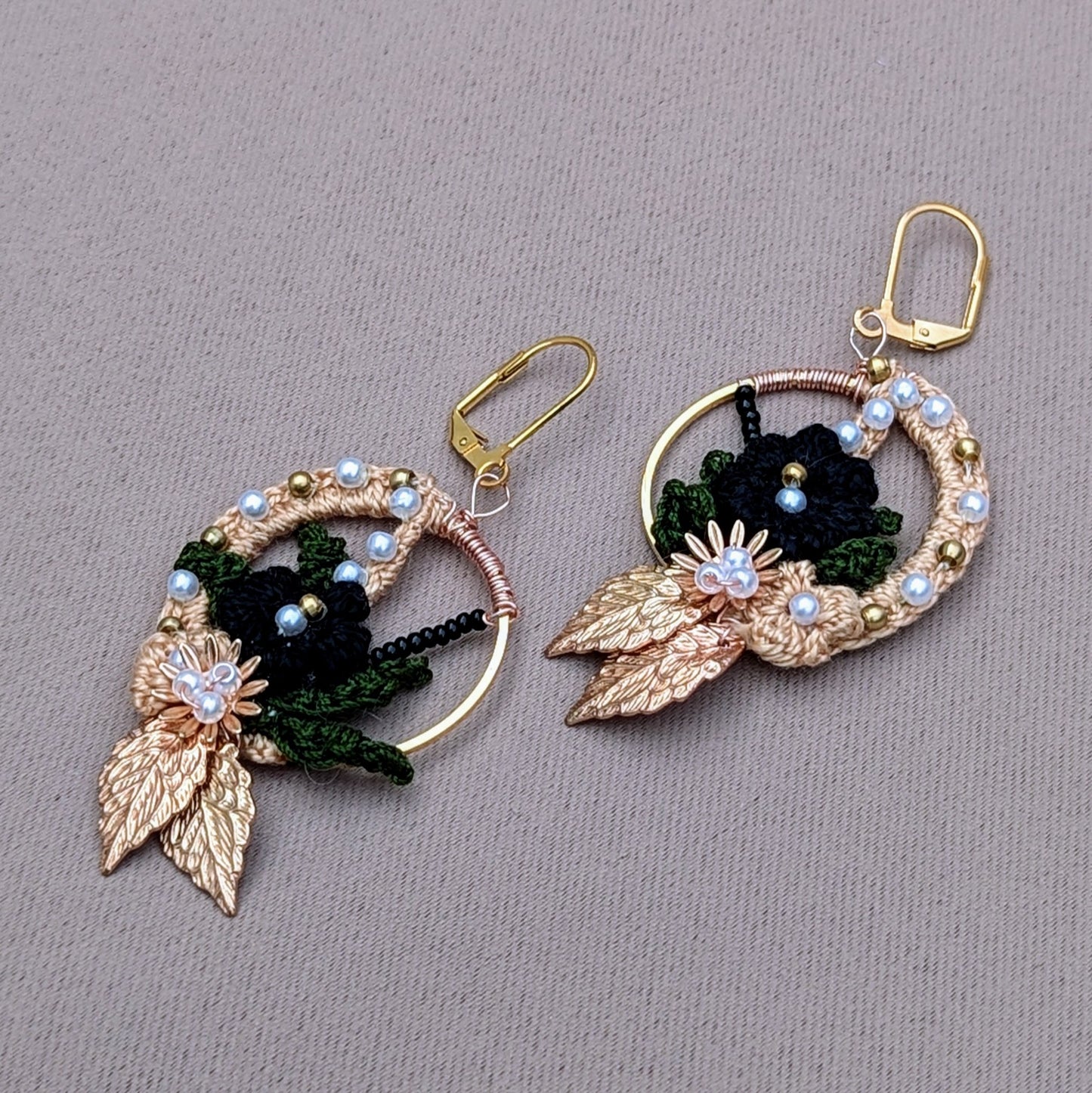 Aloki black and gold floral hoop earrings, handcrafted with crochet, seed pearls, brass beads, and gold-plated leaves.