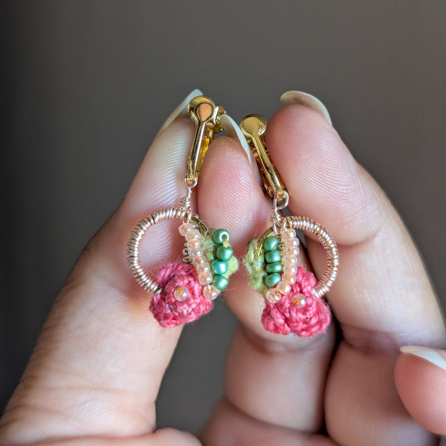 Anandi lightweight clip-on earrings by Mayaani Jewellery featuring rose pink crochet flowers with an abundance of rose gold plated wire wrapped around a gold hoop and chartreuse see bead detailing.
