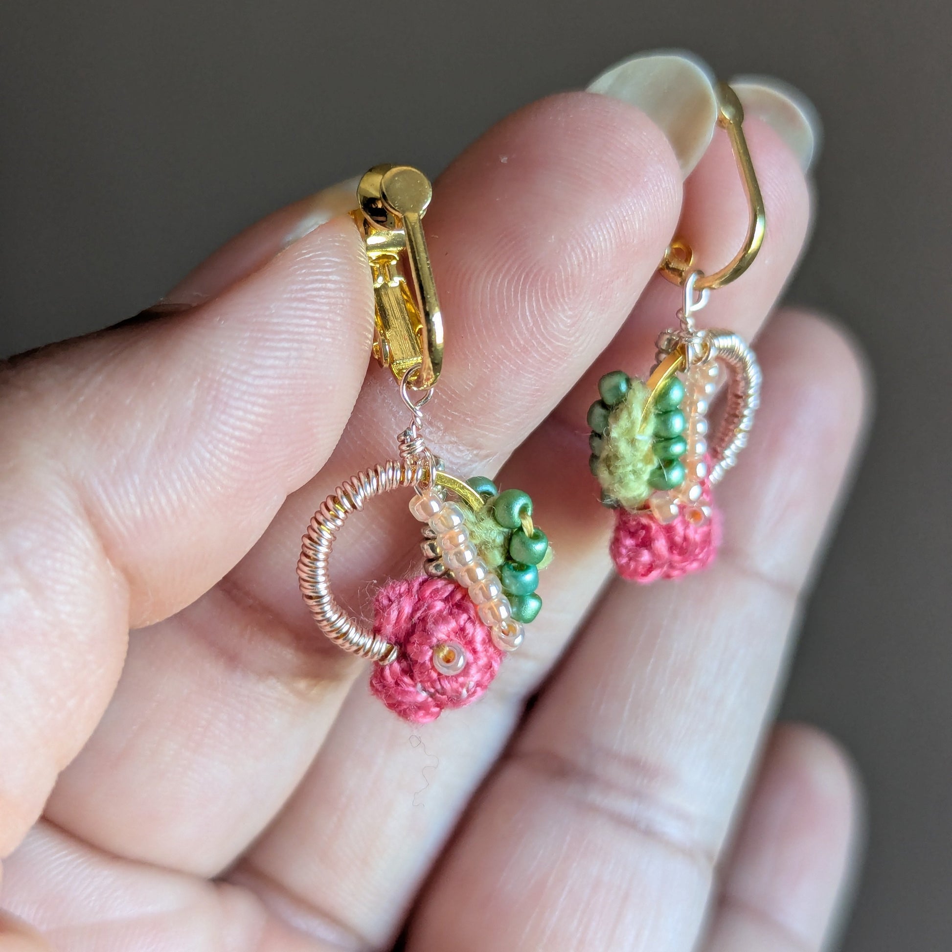 Hand holding the Anandi hand woven pink, green and gold playful floral inspired clip-on earrings from sustainable UK brand Mayaani Jewellery. 