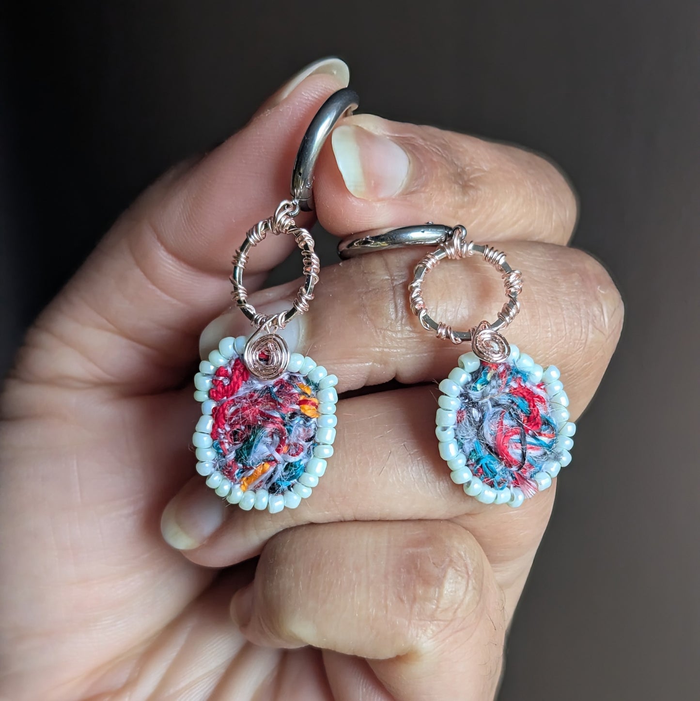 Close-up of one-of-a-kind scrap bead textile art earrings with silver hoop and wire wrapped detail.