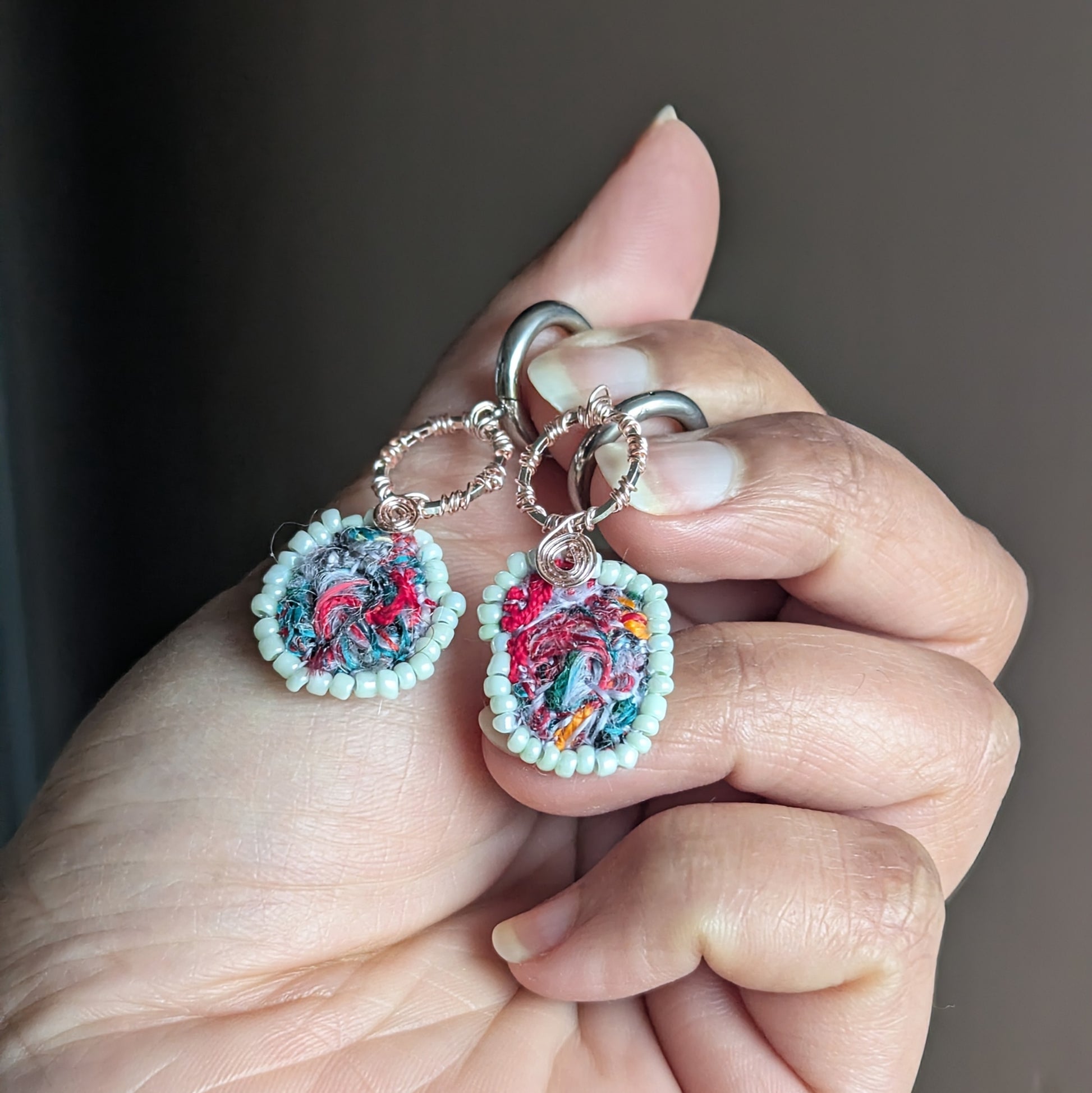 Hand holding asymmetric sustainable earrings featuring abstract textile scrap centres.