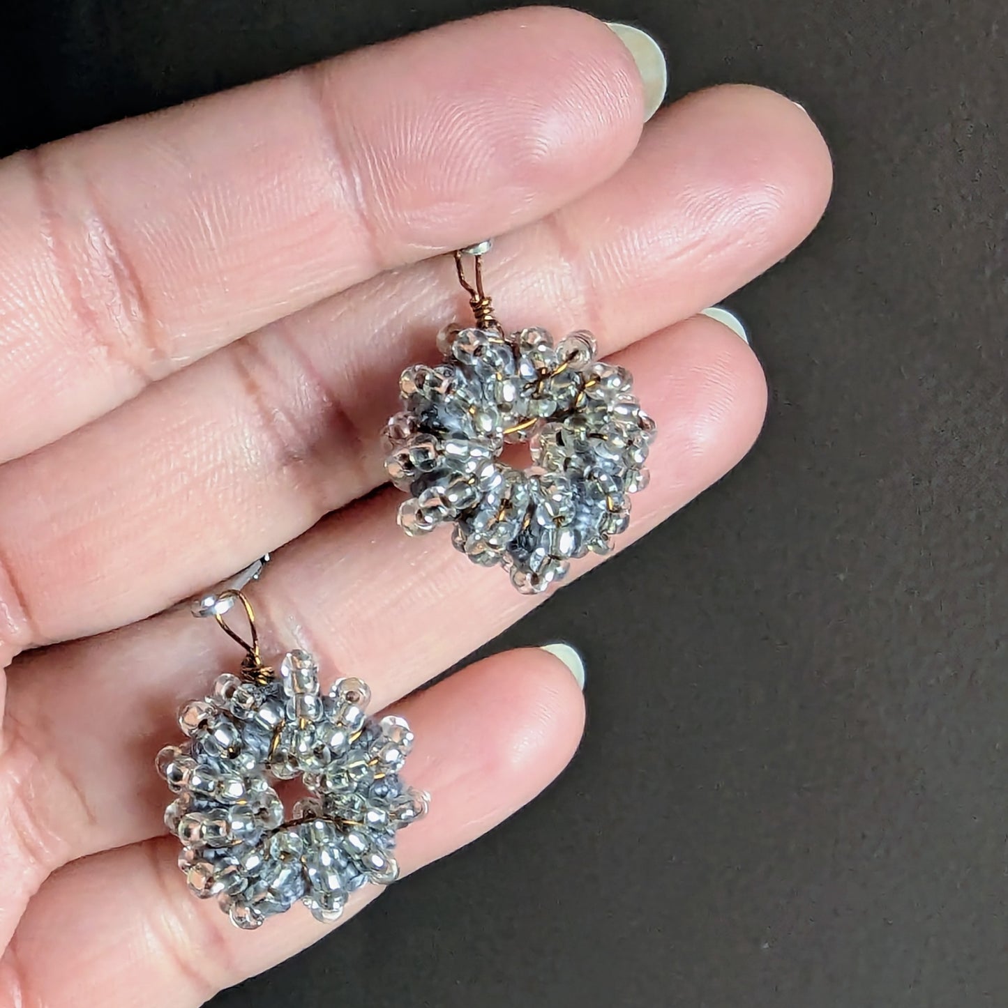 Hand holding silver-grey handmade beaded earrings crafted by Mayaani Jewellery UK.