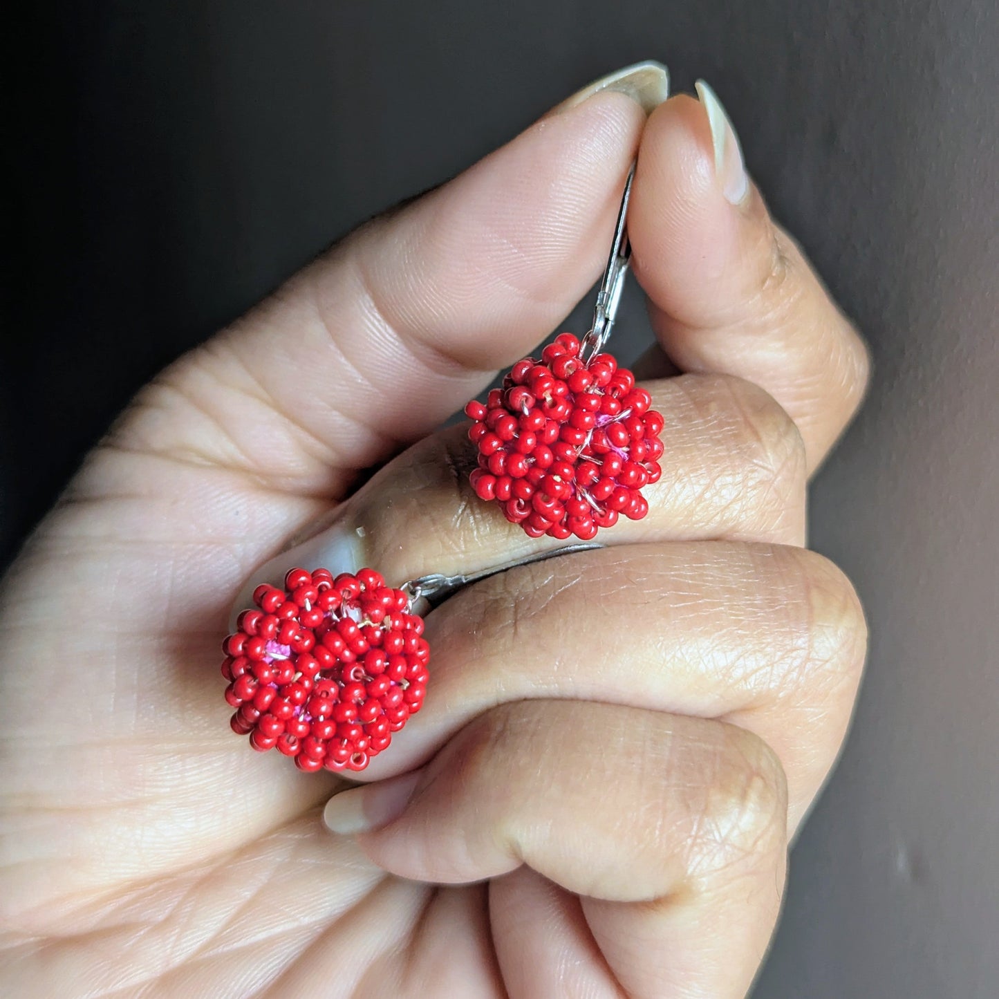 Hand holding a pair of handmade red beaded cluster earrings from Mayaani Jewellery, crafted with Czech glass beads and rose-gold wire.
