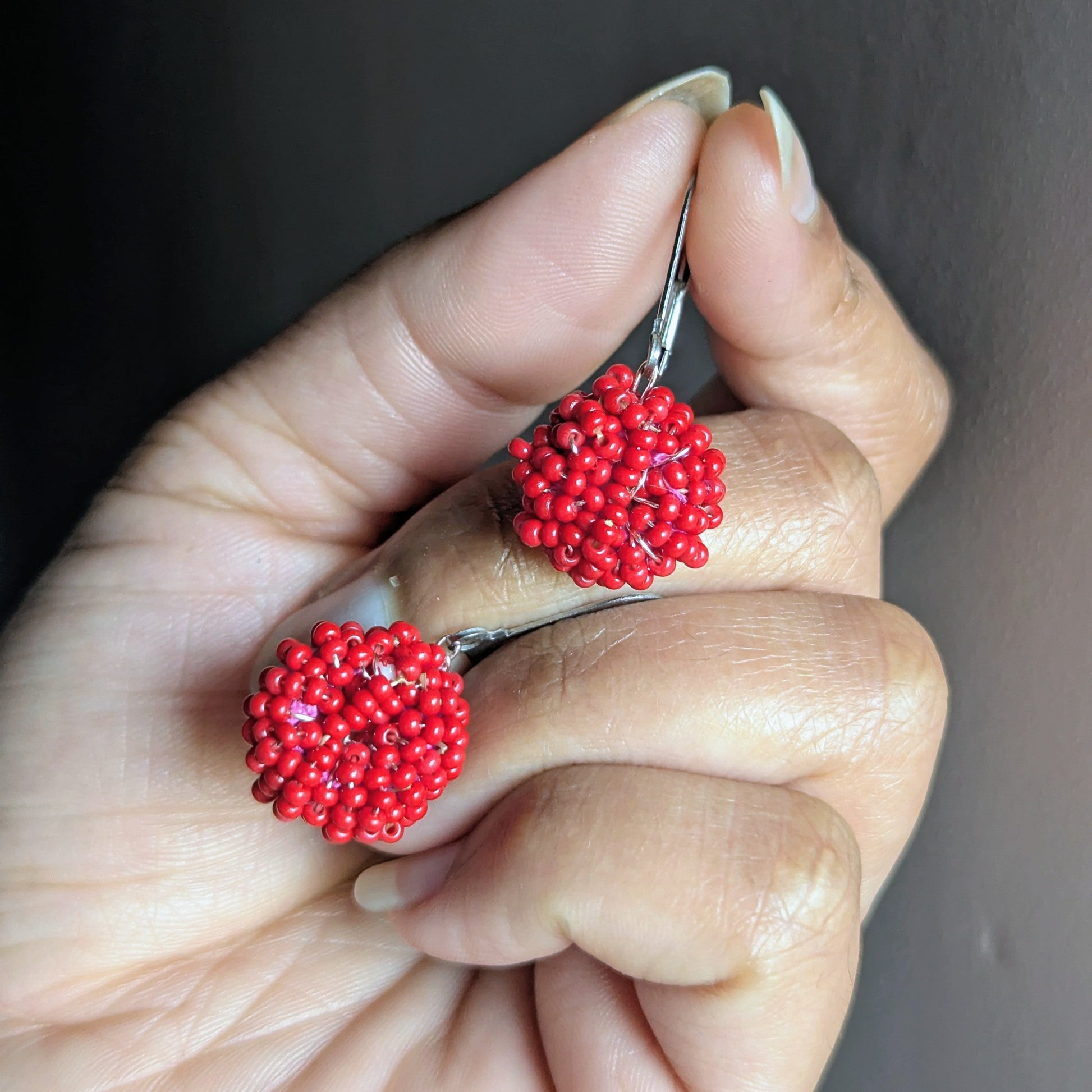 Hand holding a pair of handmade red beaded cluster earrings from Mayaani Jewellery, crafted with Czech glass beads and rose-gold wire.
