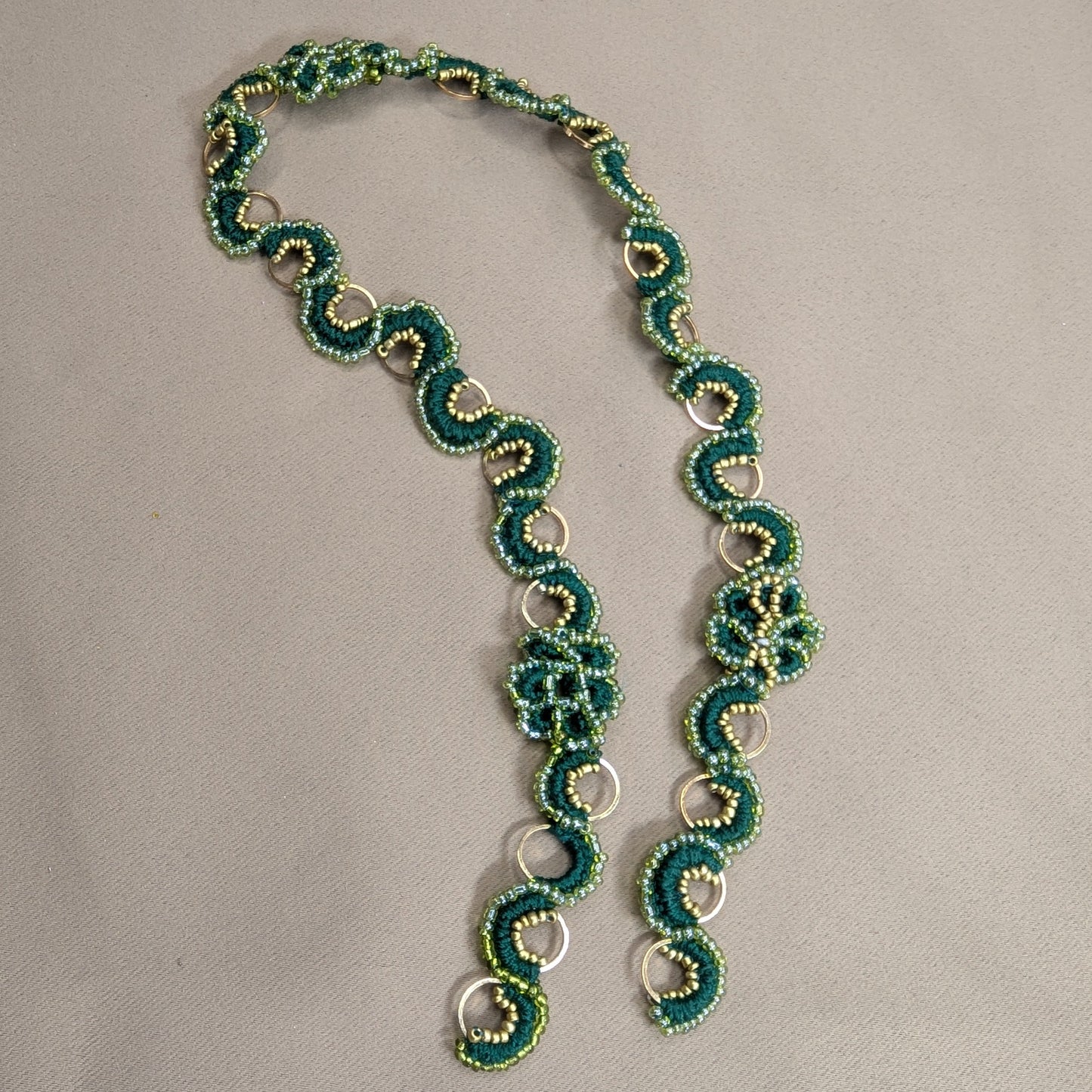 Rukmini emerald green and gold bead crochet handmade chain on a neutral grey backdrop. Custom made exclusively at Mayaani Jewellery UK.