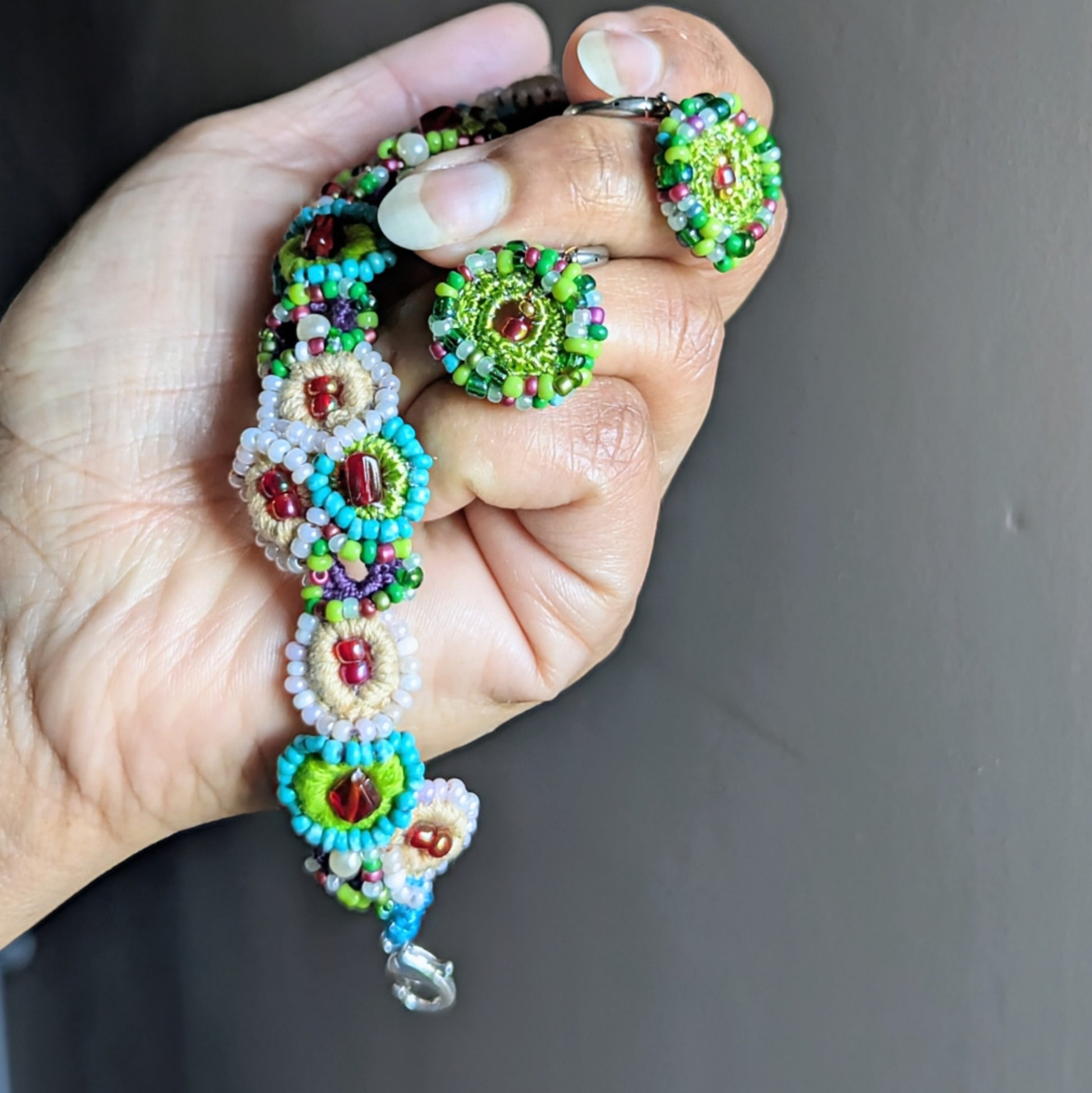 Handmade Vana garden bracelet and earrings held in hand, featuring bead crochet florals in green, blue, ivory and red, sustainable Indian artisan jewellery.