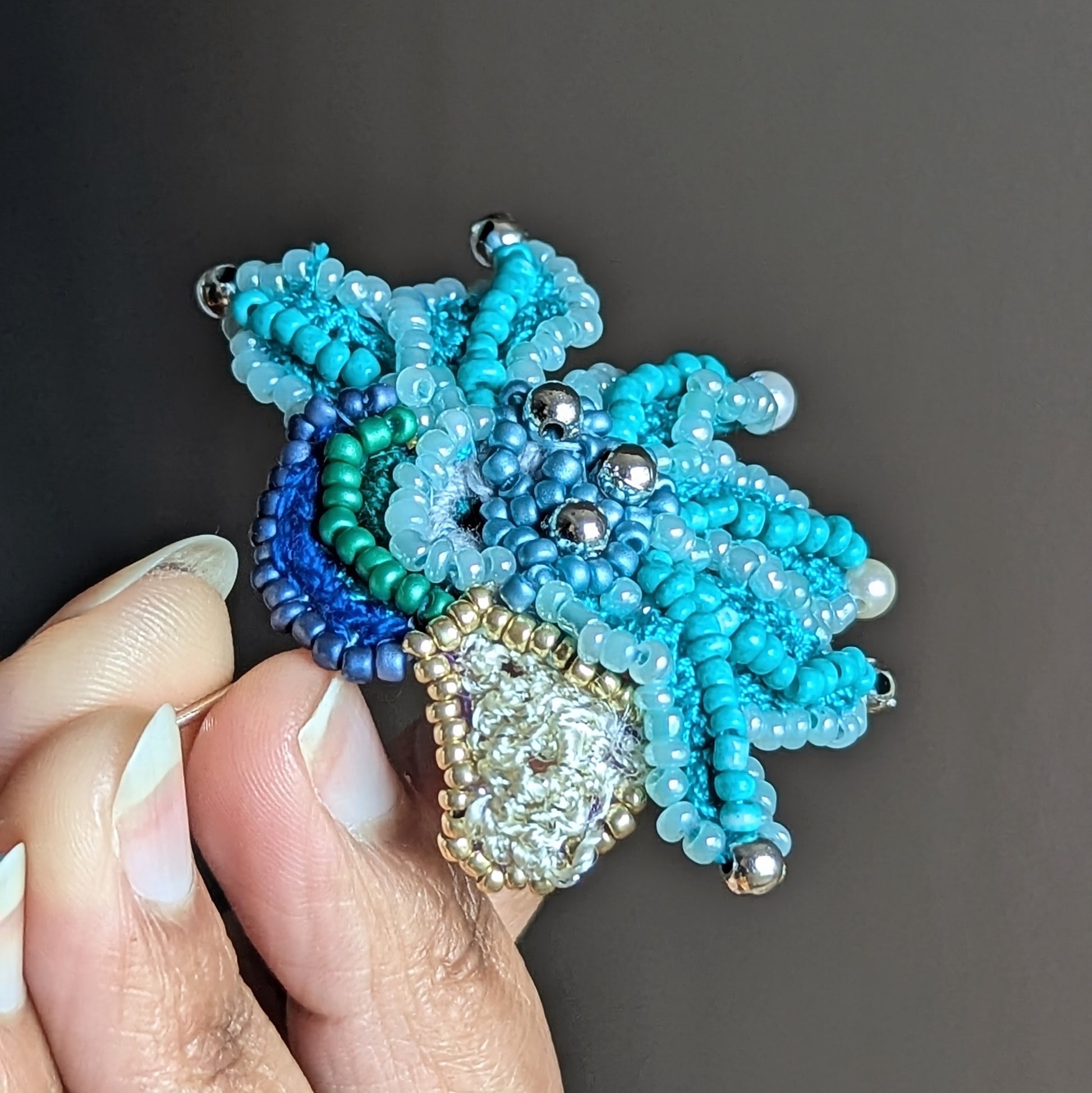 Handcrafted turquoise beaded brooch Jalika held at an angle, in hand, highlighting turquoise beadwork and sustainable artisan craftsmanship.