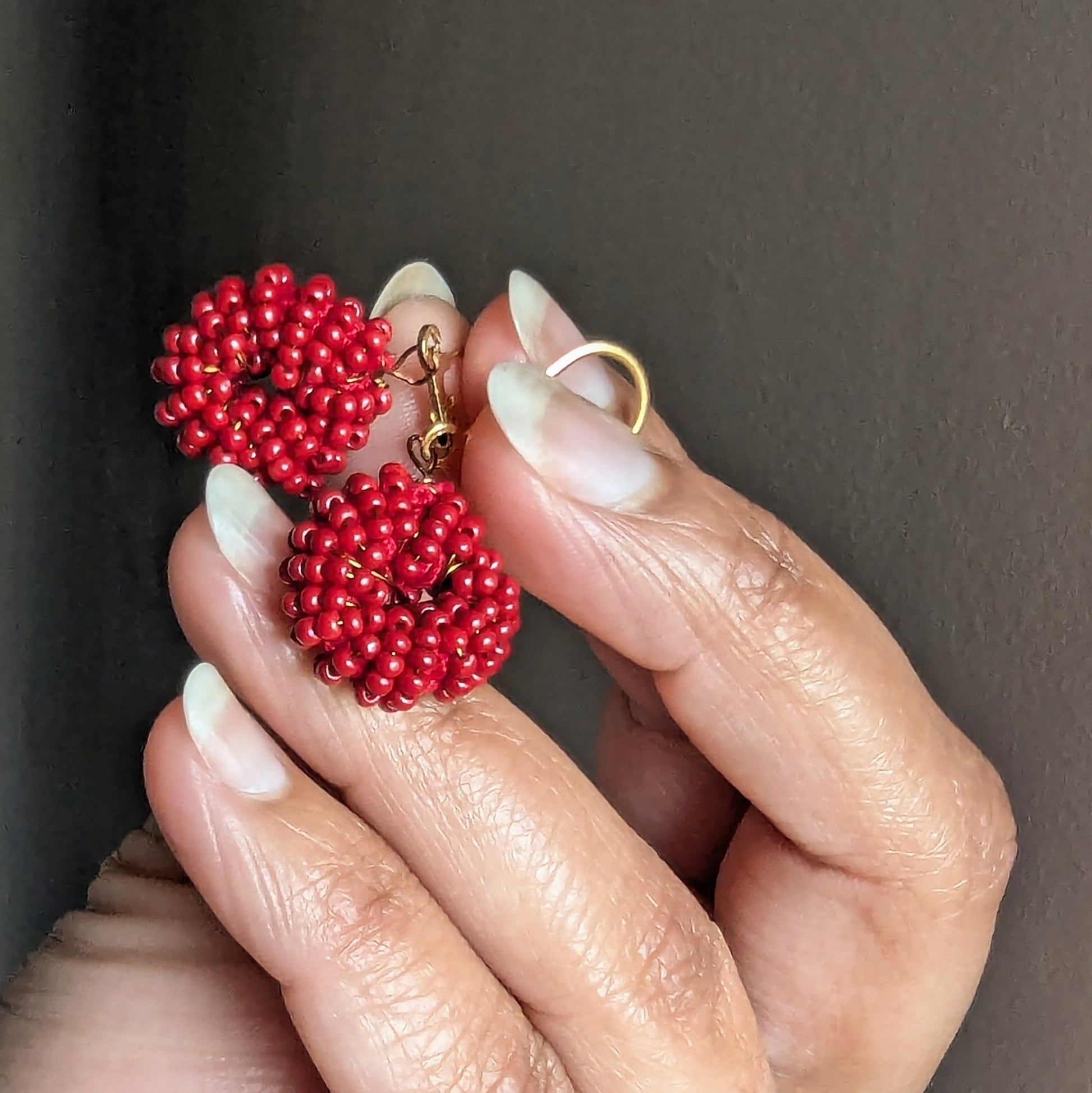 Red beaded earrings held by a hand against a dark background made for designer brand Mayaani.