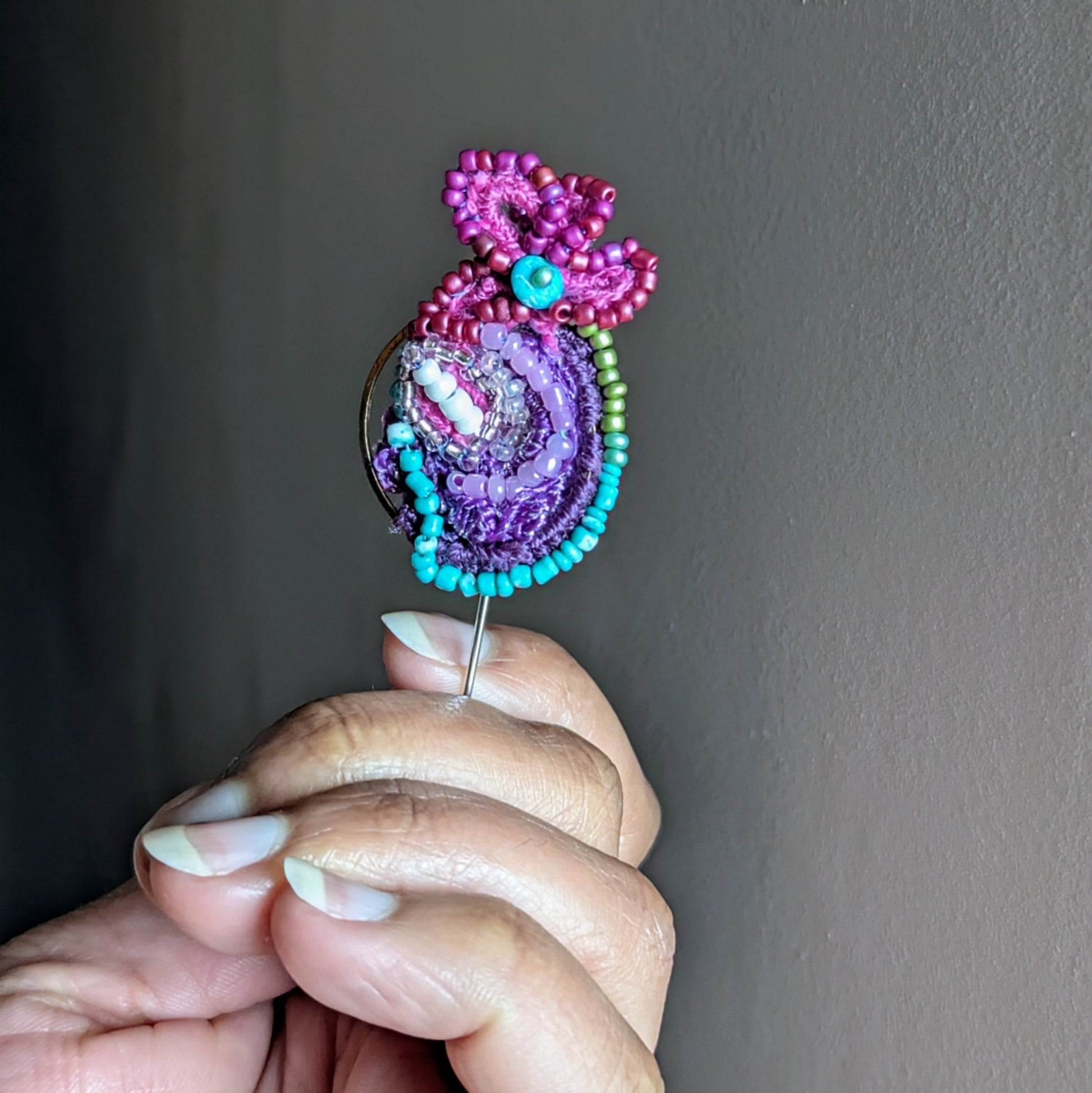 Close up angled view of Navira sustainable handmade brooch featuring layered vintae and new Czech and Japanese glass seed beads in purple, teal and fuschia with stainless steel pin fastening.