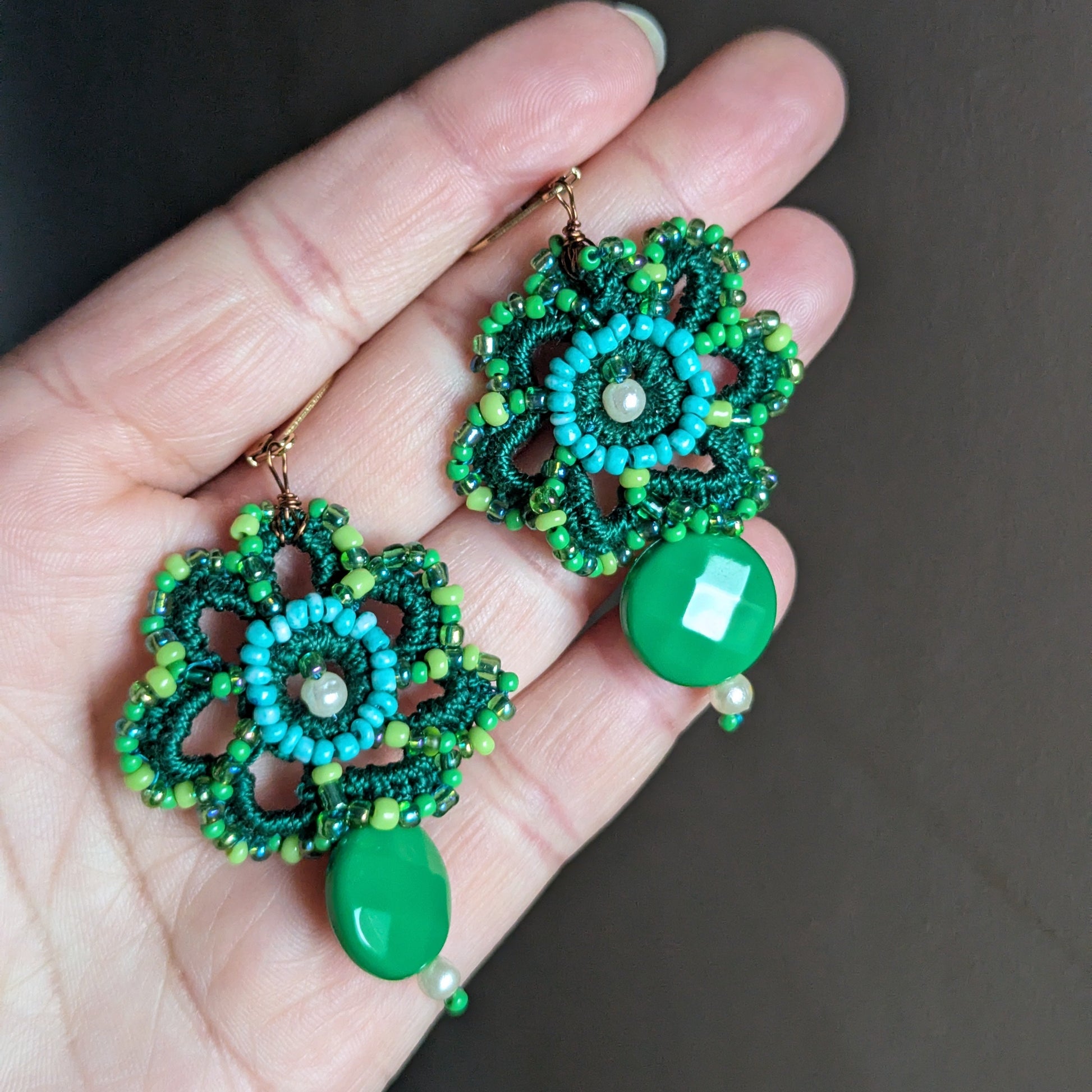 Avika green floral crochet earrings held in hand featuring layered vintage seed beads, turquoise centre detail and glossy green bead drop.
