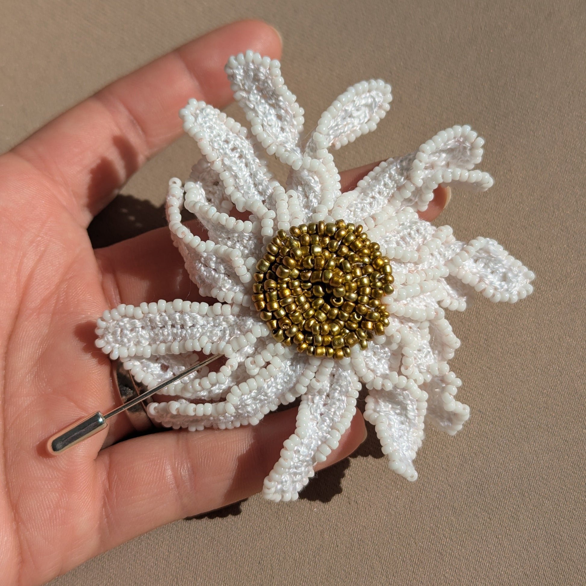 Close up view of a handmade daisy floral brooch lapel hat pin held in hand in natural daylight sustainably handmade for Mayaani Jewellery by UK Indian designer and artisan Megha.