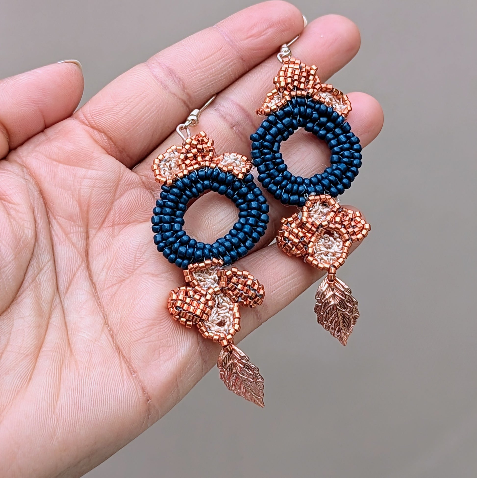Hand holding a one-of-a-kind statement pair of blue, rose gold and copper dangle drop earrings designed for luxury with comfort for Mayaani Jewellery UK.