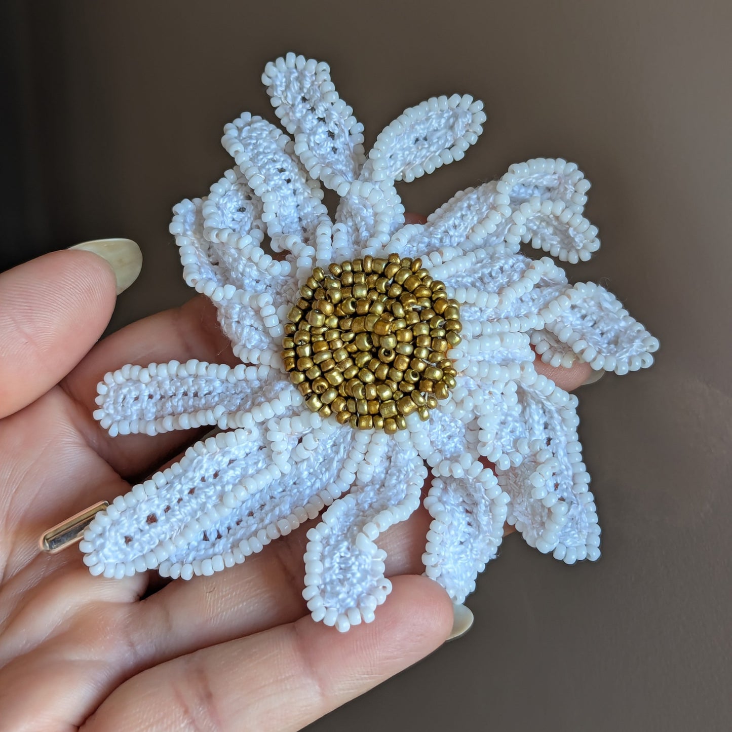 Large white and gold daisy flower brooch pin for women held in hand against a neutral backdrop.
