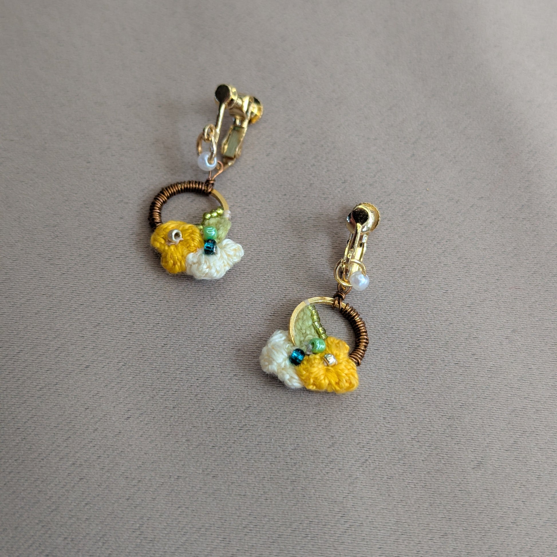 A one of a kind pair of comfortable clip-on Sauri earrings artisan handcrafted by Mayaani Jewellery UK in gold, yellow, green, pearl and bronze.