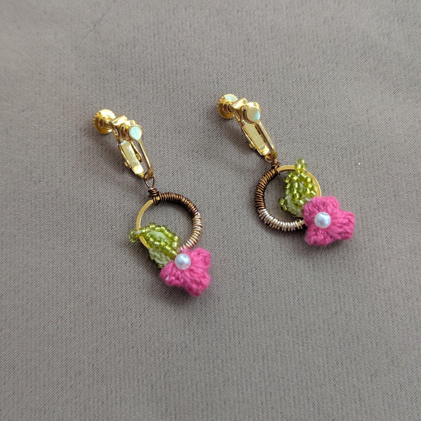 Close up view of a couture pair of intricately hand crochet, hand wire wrapped, hand bead embroidered floral motif pink, chartreuse green, gold, rose gold and bronze clip-on earrings designed for comfortable long lasting wear.