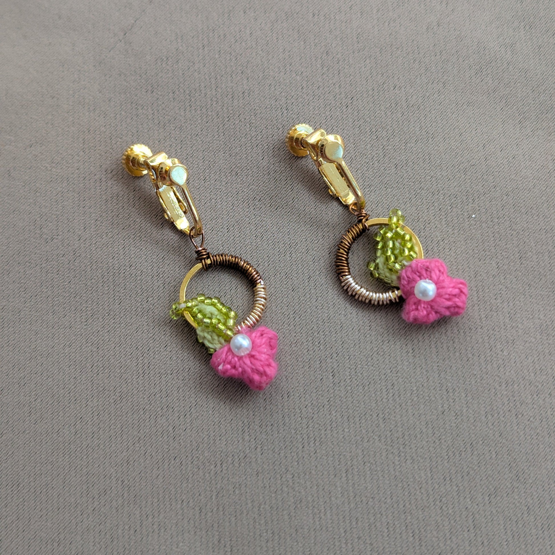 Close up view of a couture pair of intricately hand crochet, hand wire wrapped, hand bead embroidered floral motif pink, chartreuse green, gold, rose gold and bronze clip-on earrings designed for comfortable long lasting wear.