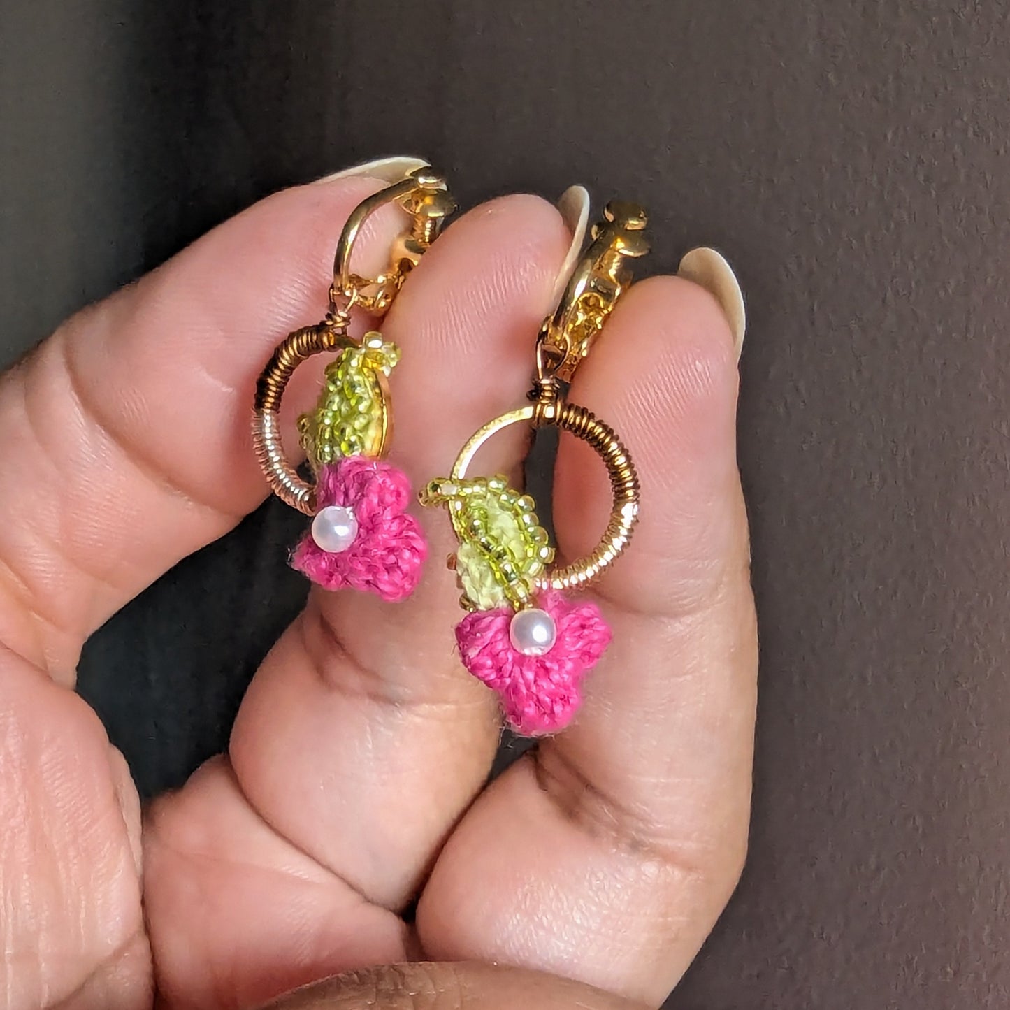 A hand holding a dainty pair of small lightweight comfortable Pallavi gold, green, pink and pearl earrings suitable for anyone without ear piercings for comfortable heirloom quality wear.