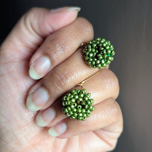 Hand holding a pair of soft green handmade seed bead earrings crafted by Mayaani Jewellery UK.