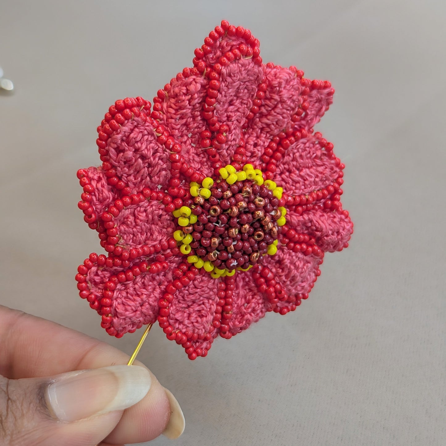 Zinnia handmade artisan brooch side view showing detailed layered crochet and seed bead work and gold-plated copper brooch pin against a neutral backdrop. Designed and hand crafted for Mayaani Jewellery UK.