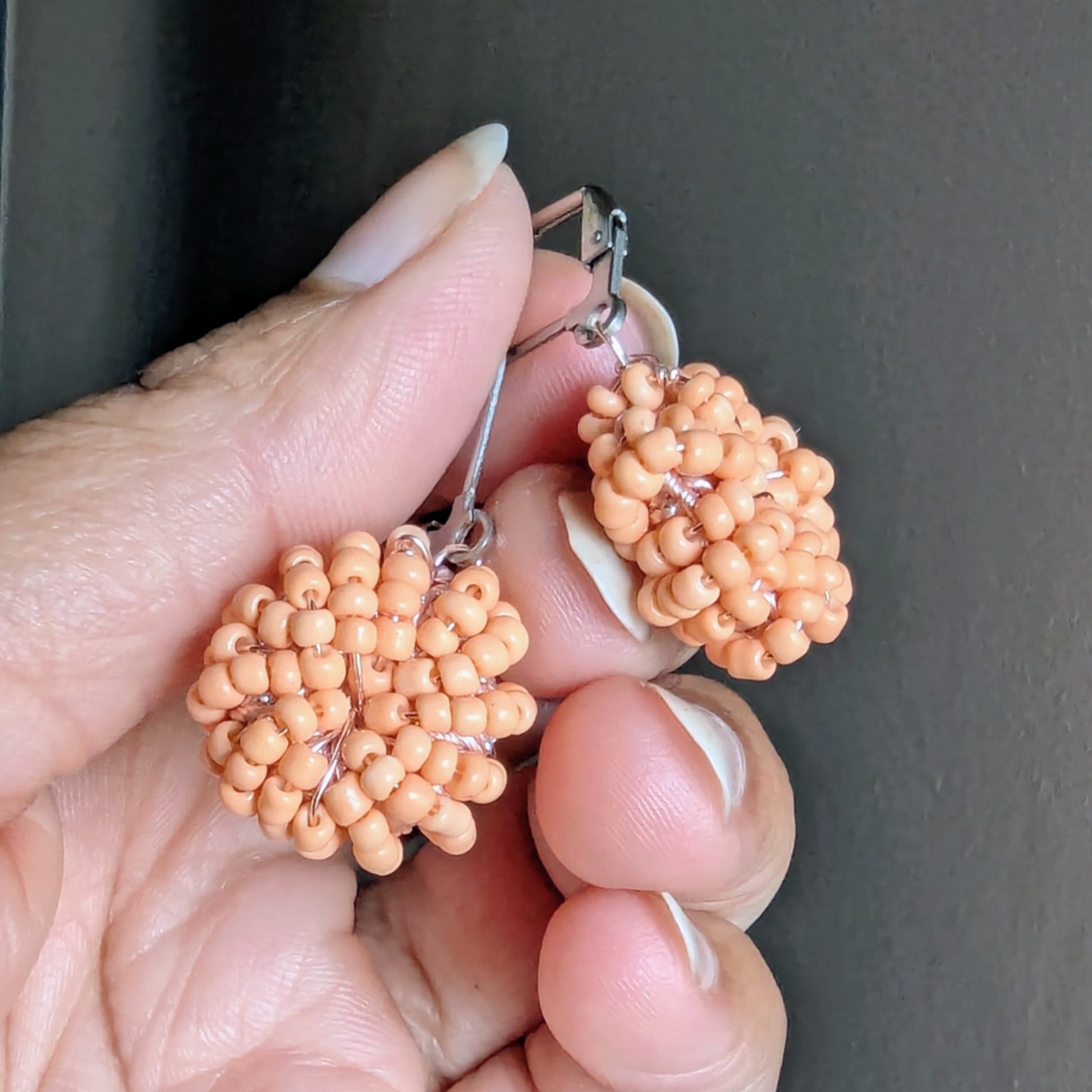 Hand holding soft peach handmade beaded earrings crafted by Mayaani Jewellery UK.