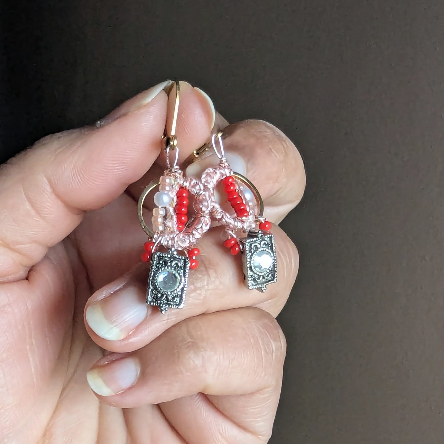Handheld photo of Inara handmade beaded earrings featuring vintage CZ charms, blush thread-wrapped loop, red seed beads and seed pearls on gold stainless steel rings and clasps.