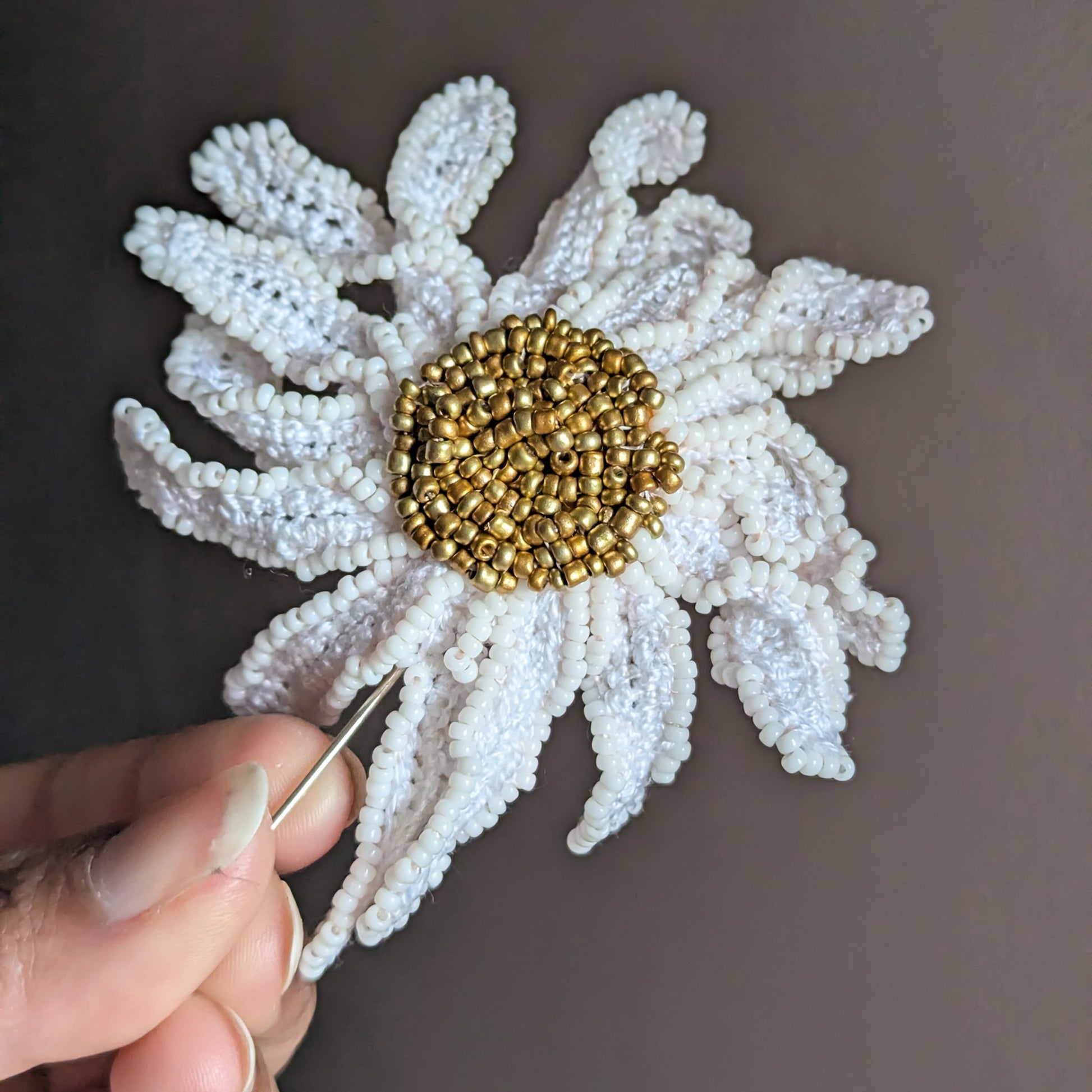 Radiant daisy flower garden inspired brooch pin held in hand against a dark grey neutral backdrop.